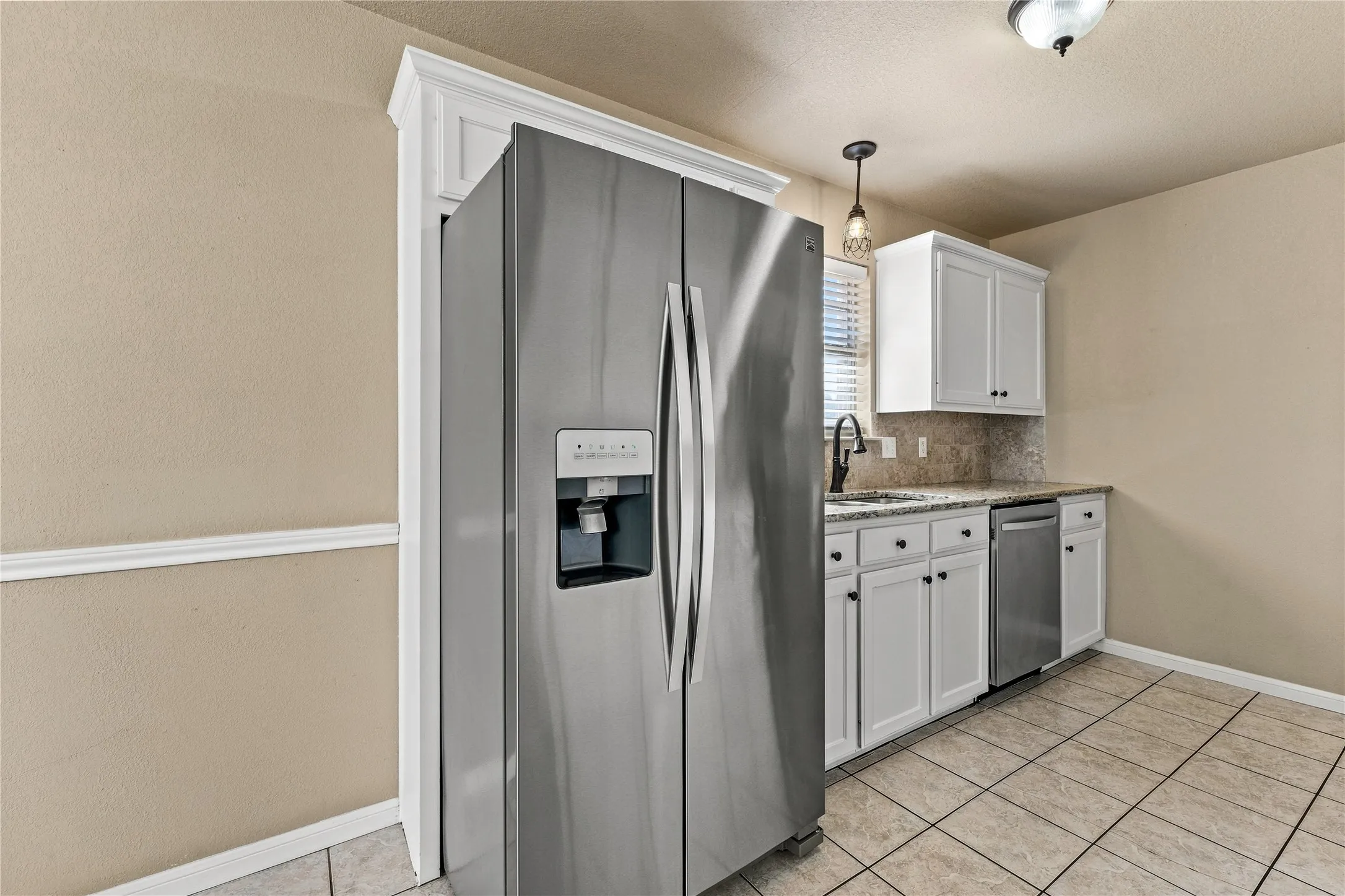 Built-in stainless steel refrigerator, white cabinetry, polished countertop, stainless steel dishwasher, and tile flooring