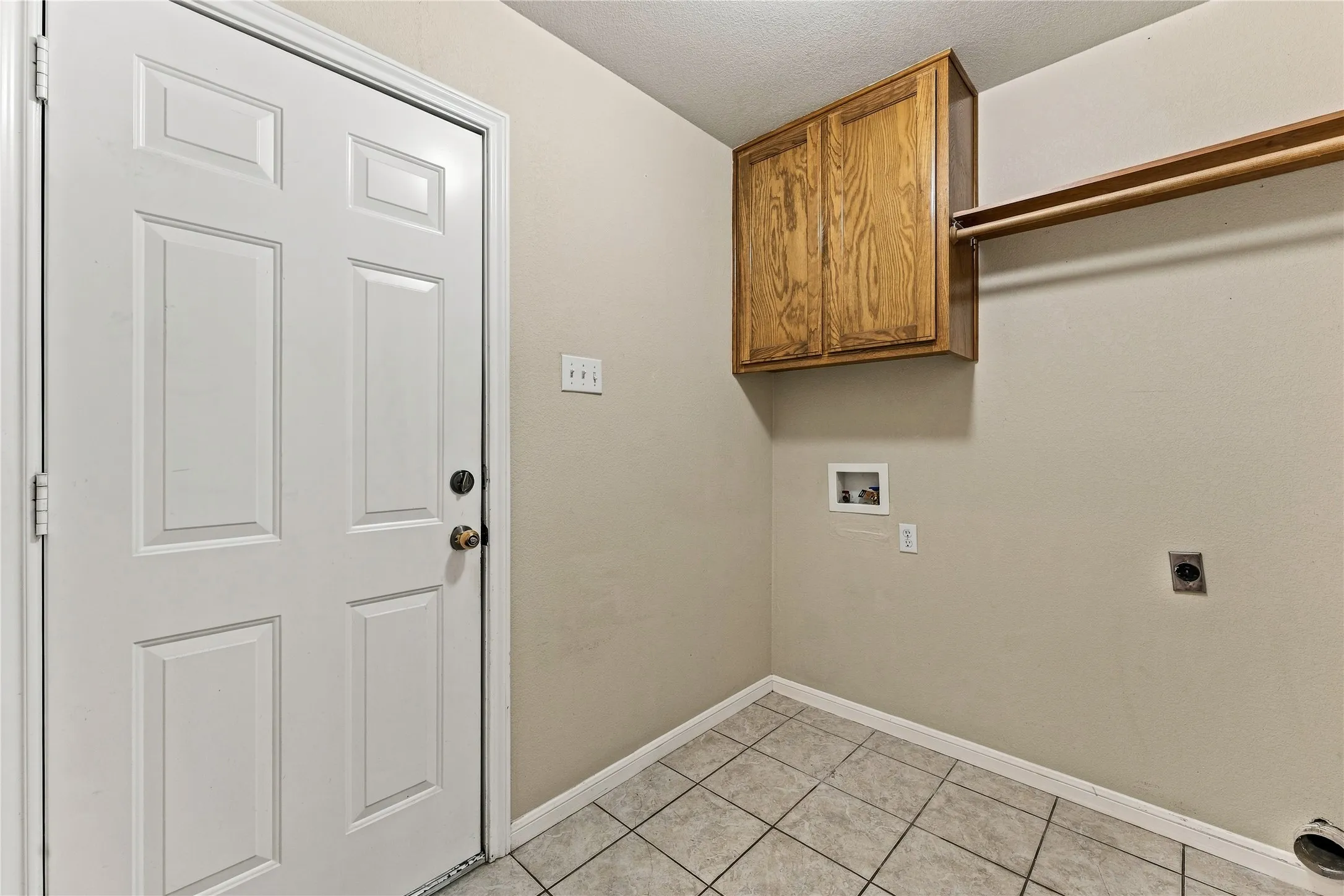 Tiled flooring, overhead wood cabinetry, and a wall-mounted clothes rod