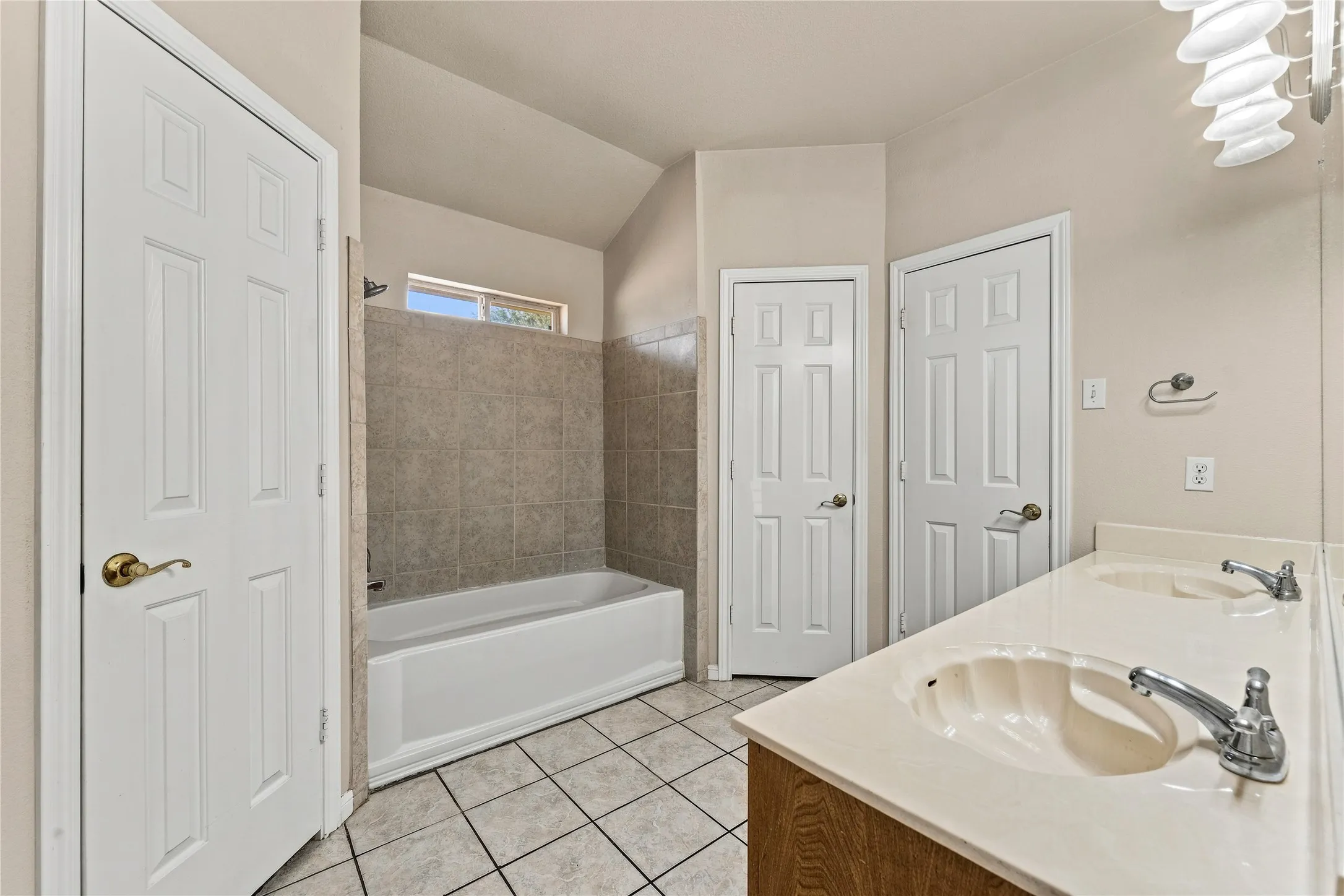Dual vanity with integrated sinks, tiled flooring, bathtub with tiled surround, and multiple doors