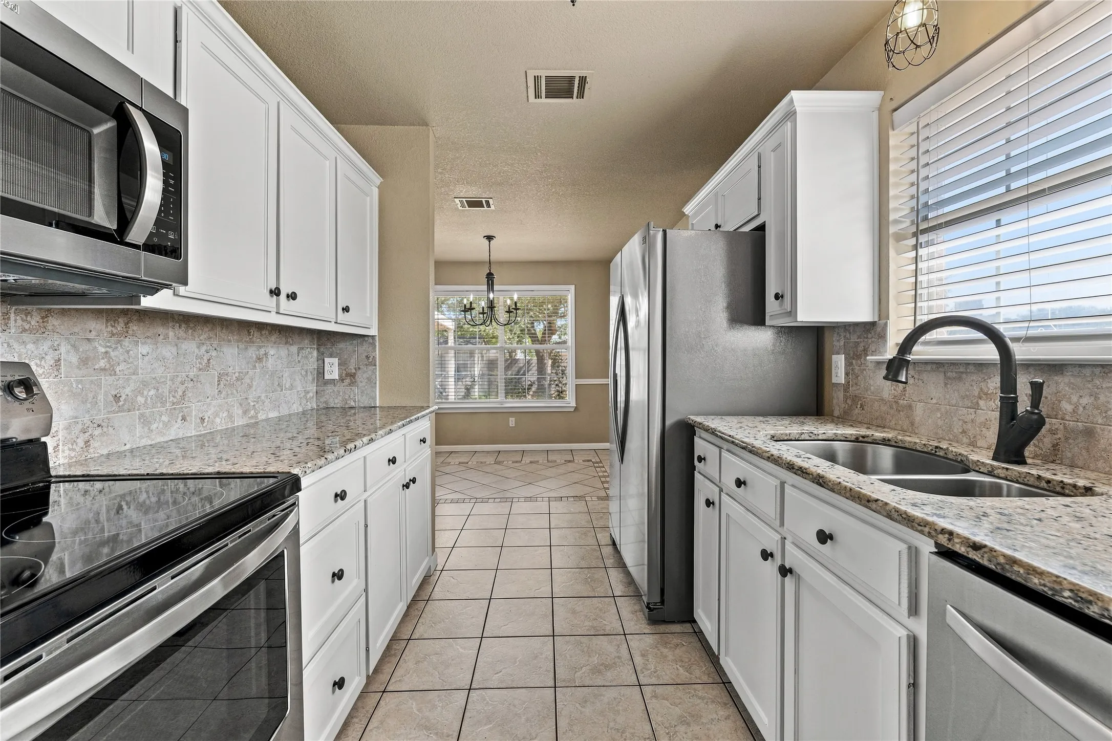 Kitchen featuring white cabinetry, granite countertops, stainless steel appliances, a tile backsplash, and tile flooring