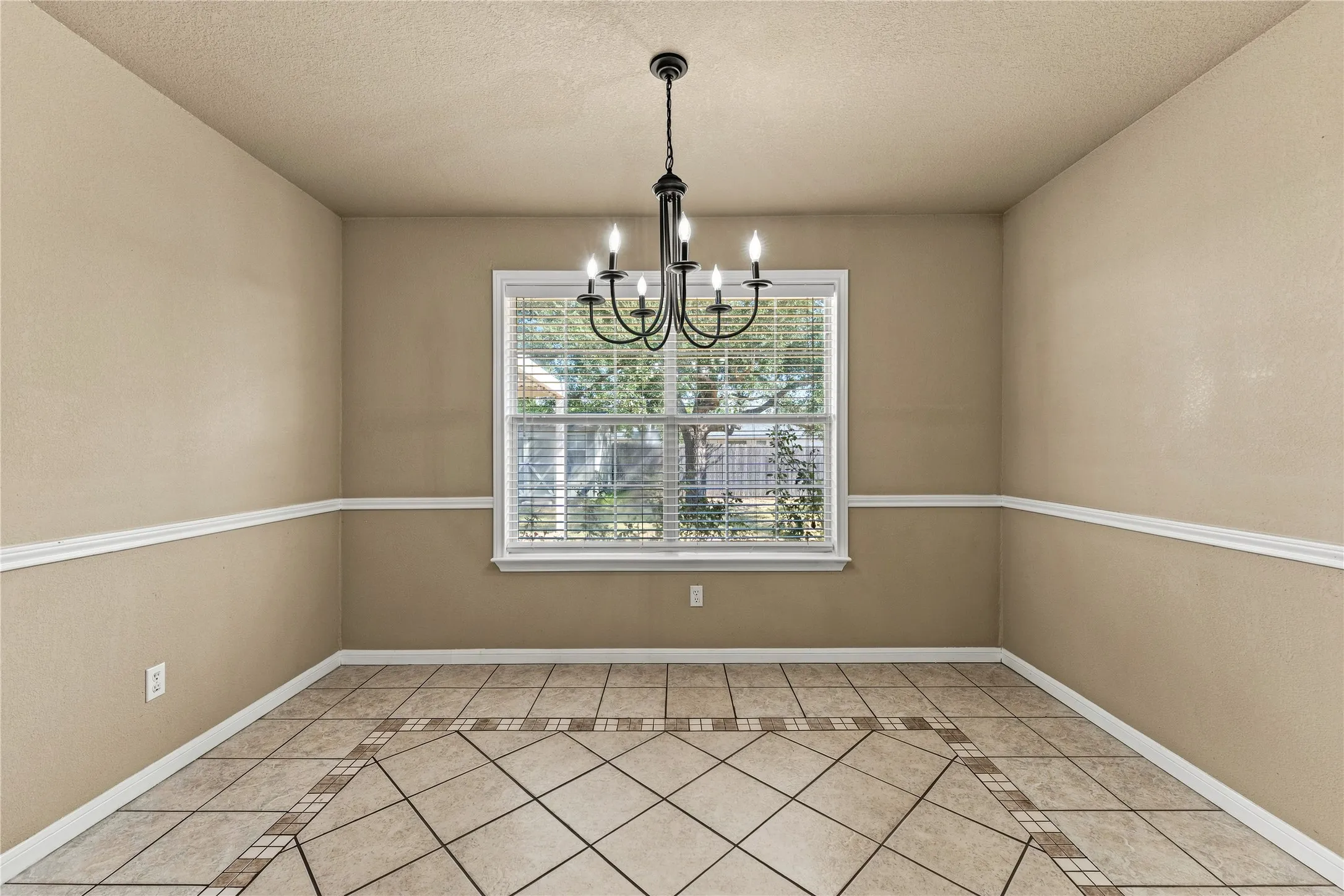 Tile flooring with an inlaid pattern, neutral wall tones, decorative chair rail molding, and a central window with blinds