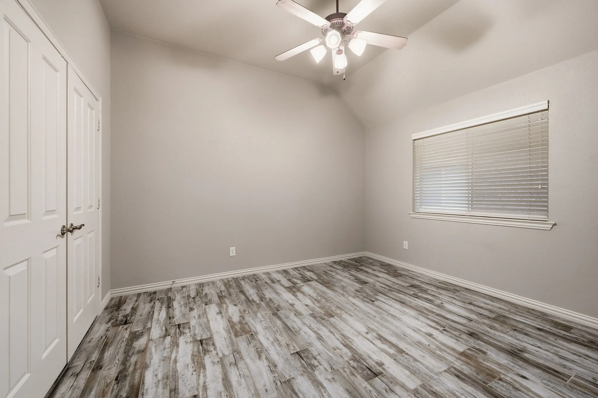 Vaulted ceiling with a ceiling fan, wood-finish flooring, and a window with blinds