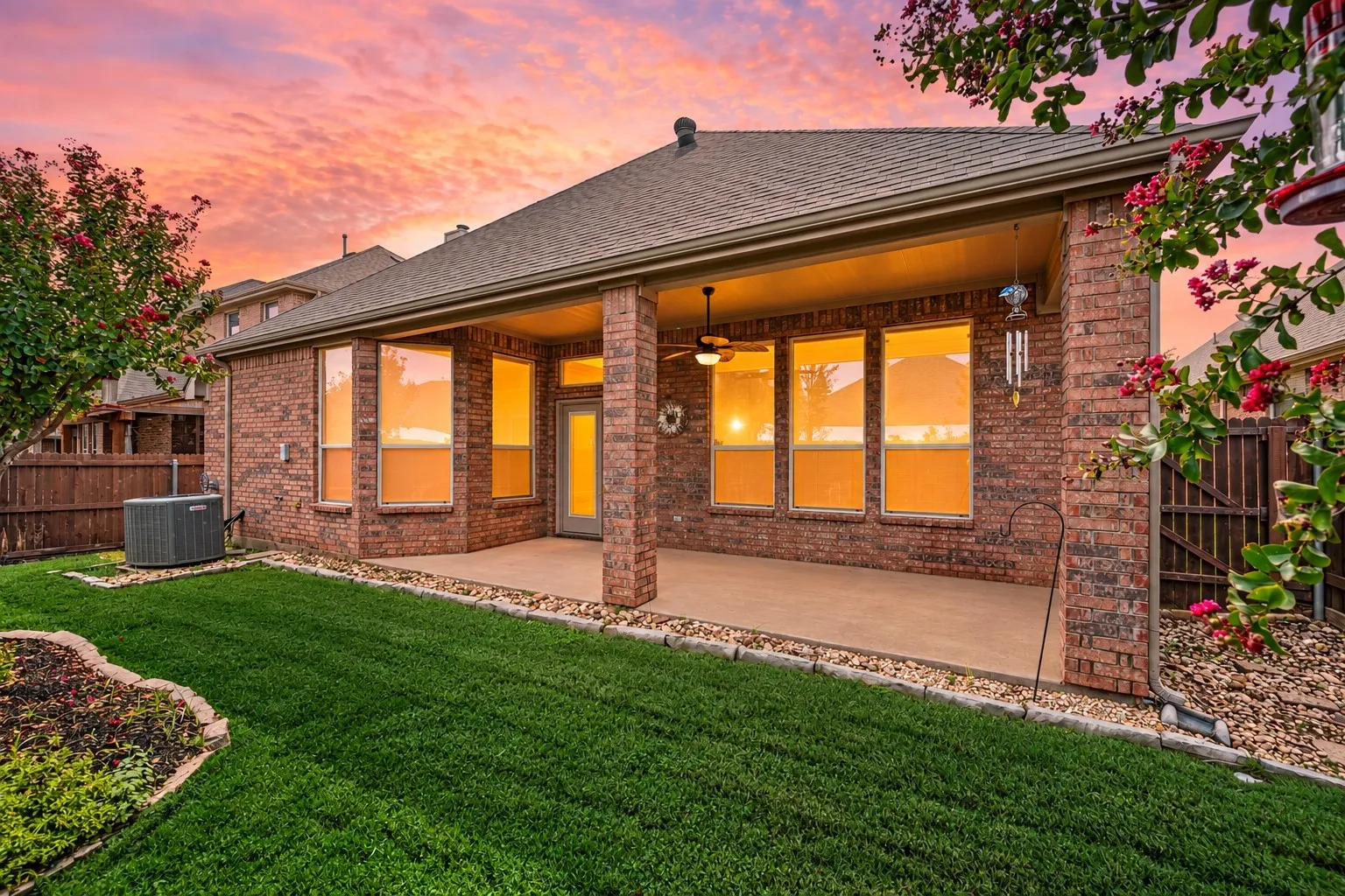 Brick exterior with covered patio featuring a ceiling fan, multiple windows, and a manicured lawn
