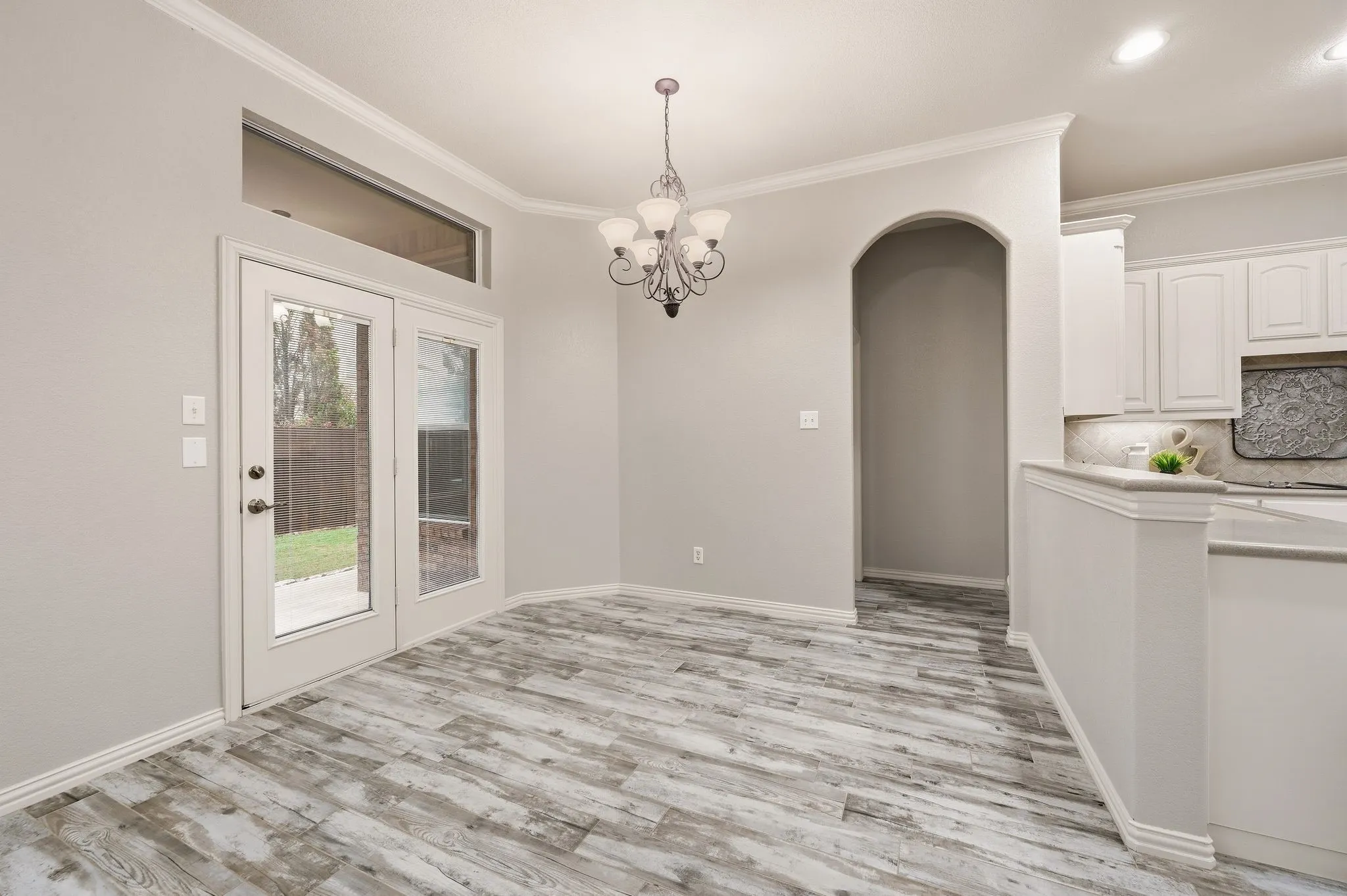 Wood-finish flooring, French doors with transom window, arched entryway, white cabinetry, and recessed lighting