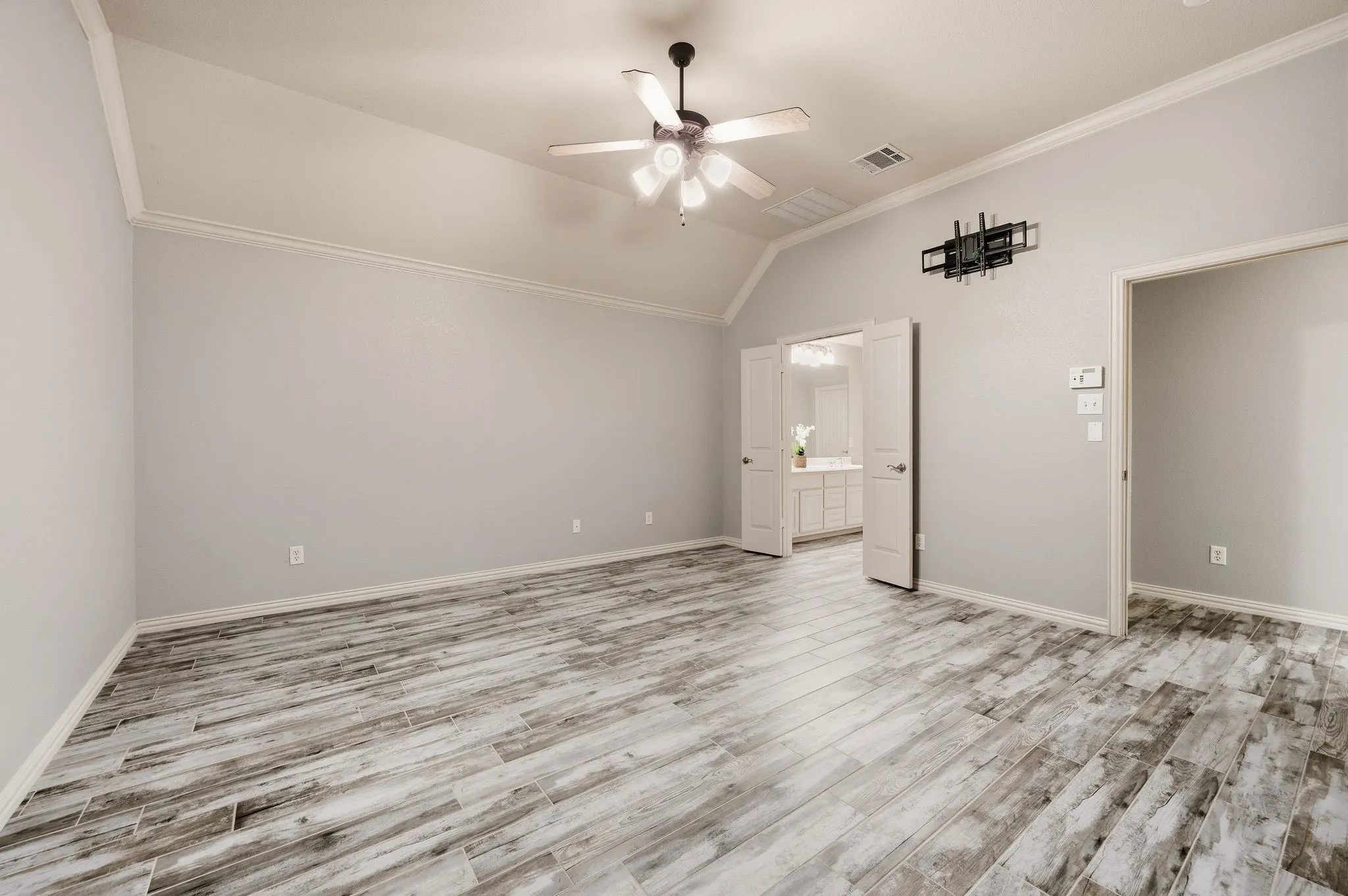 Vaulted ceiling with crown molding, ceiling fan, wood-finish flooring, and double doors