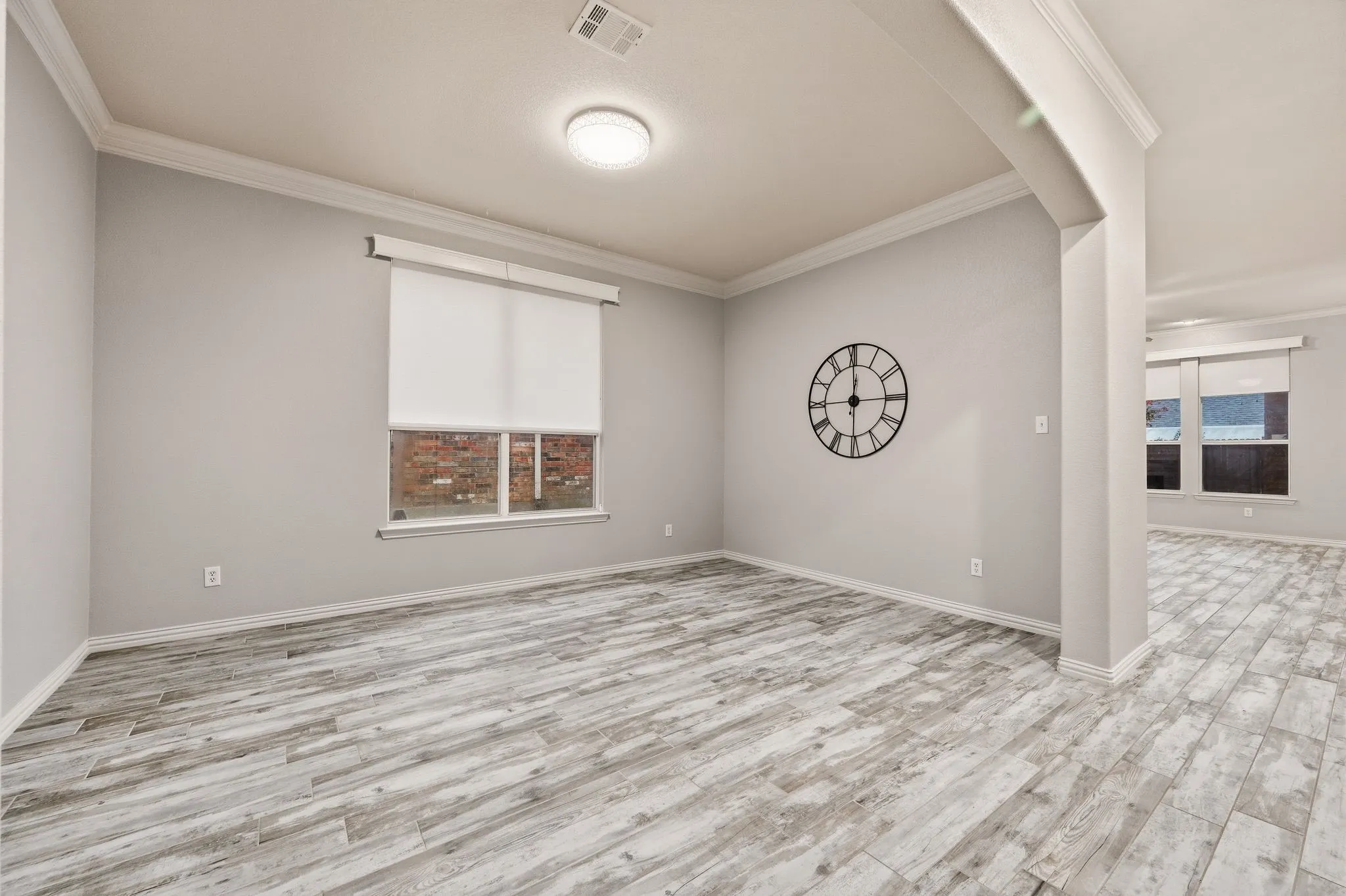 Wood-finish flooring, crown molding, recessed lighting, neutral wall tones, and window with roller shade