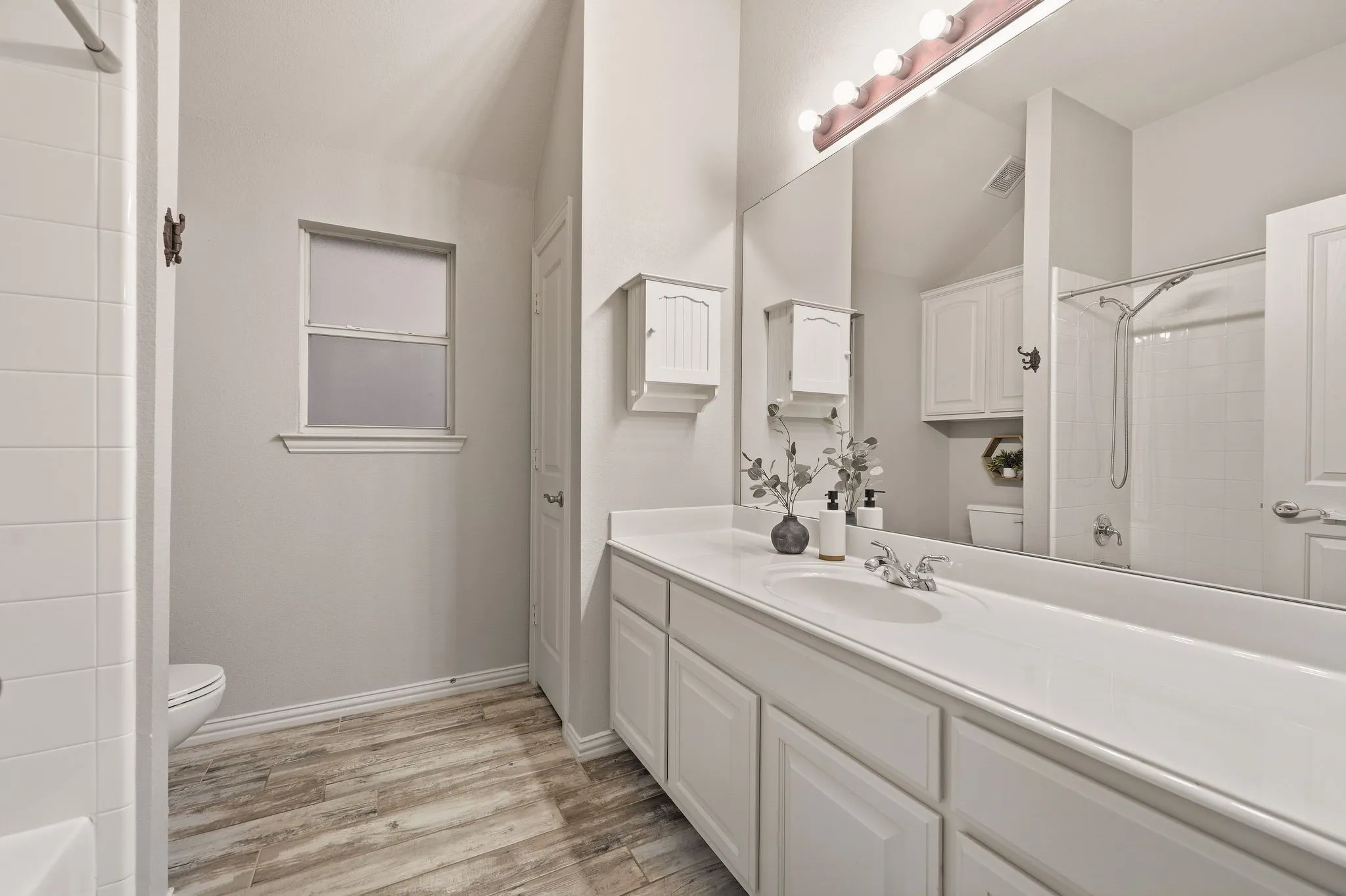 Extended vanity with integrated sink, wood-finish flooring, a combination shower and tub, and a large wall-mounted mirror