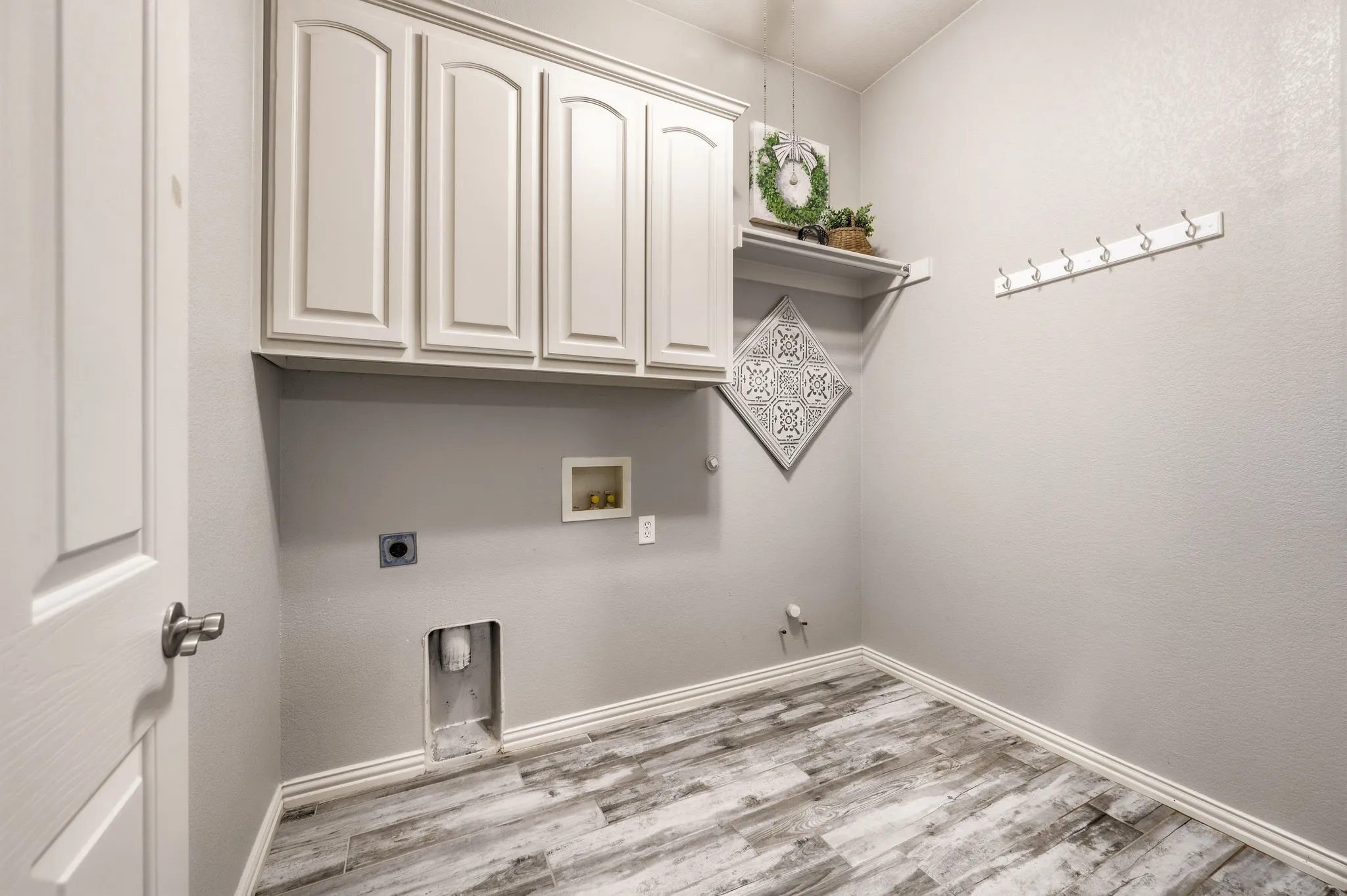 Upper cabinetry, wood-finish flooring, white trim, wall-mounted shelving, and wall-mounted hooks