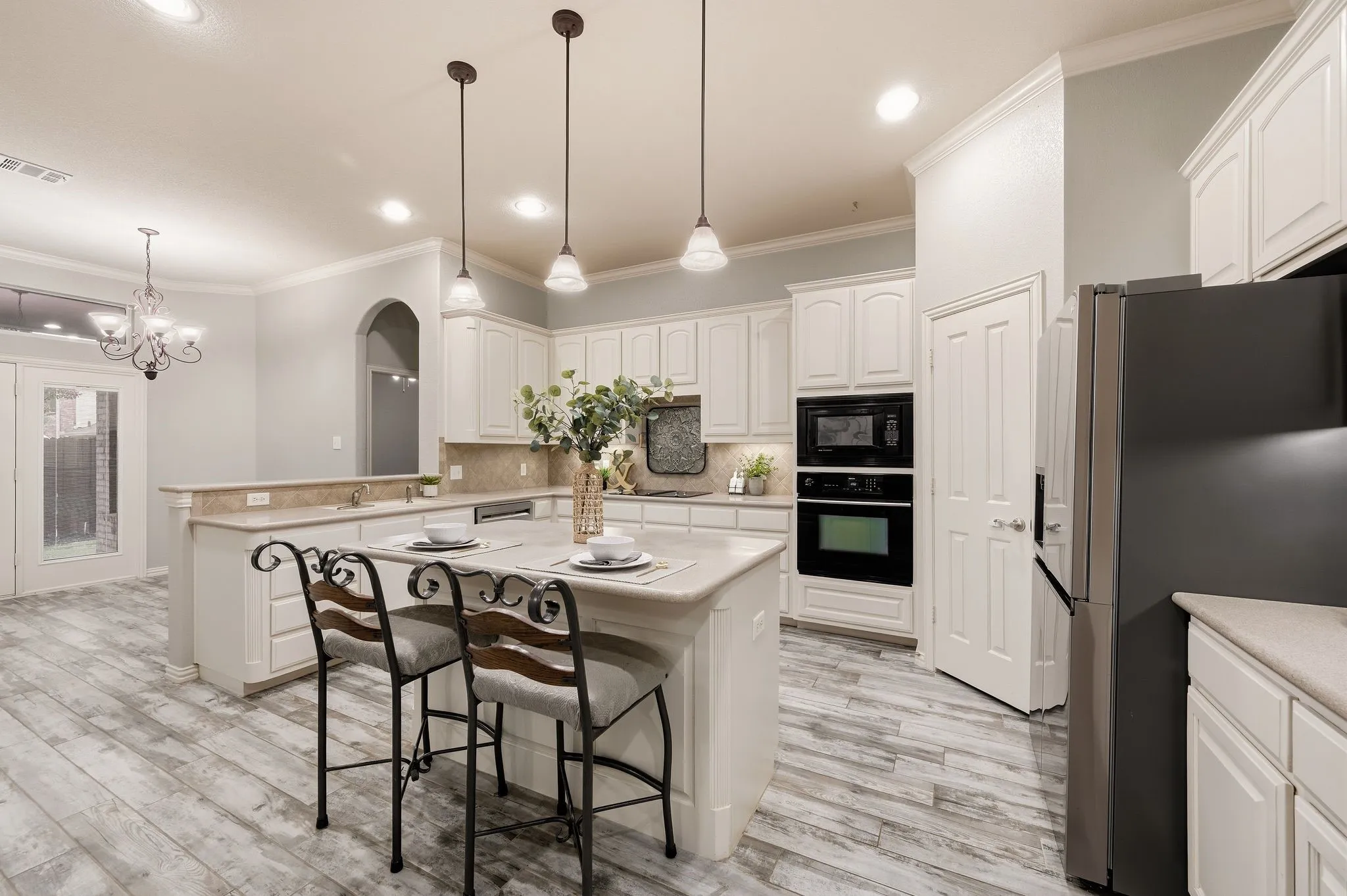 Kitchen featuring an island with pendant lighting, wood-finish flooring, built-in appliances, and white cabinetry