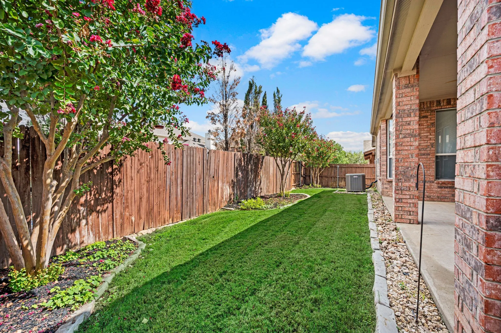 Expansive backyard featuring a manicured lawn, wood privacy fencing, and mature trees