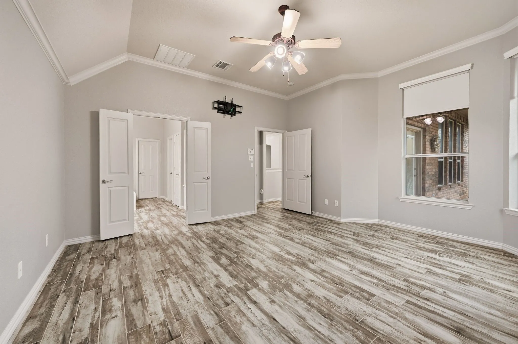 Vaulted ceiling with crown molding, wood-finish flooring, ceiling fan with integrated lighting, and multiple windows