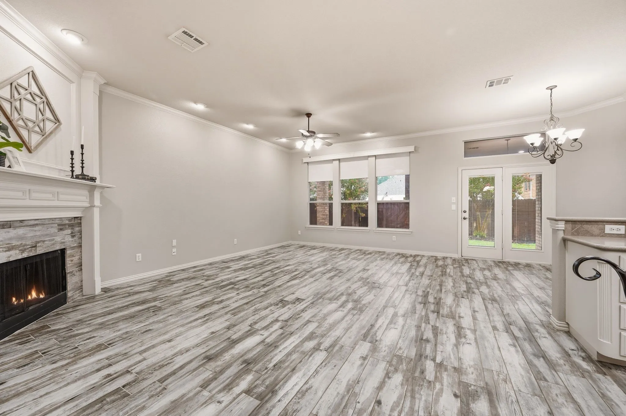 Spacious living area featuring wood-look flooring, a stone-faced fireplace with a white mantel, multiple windows, and a glass-paneled door