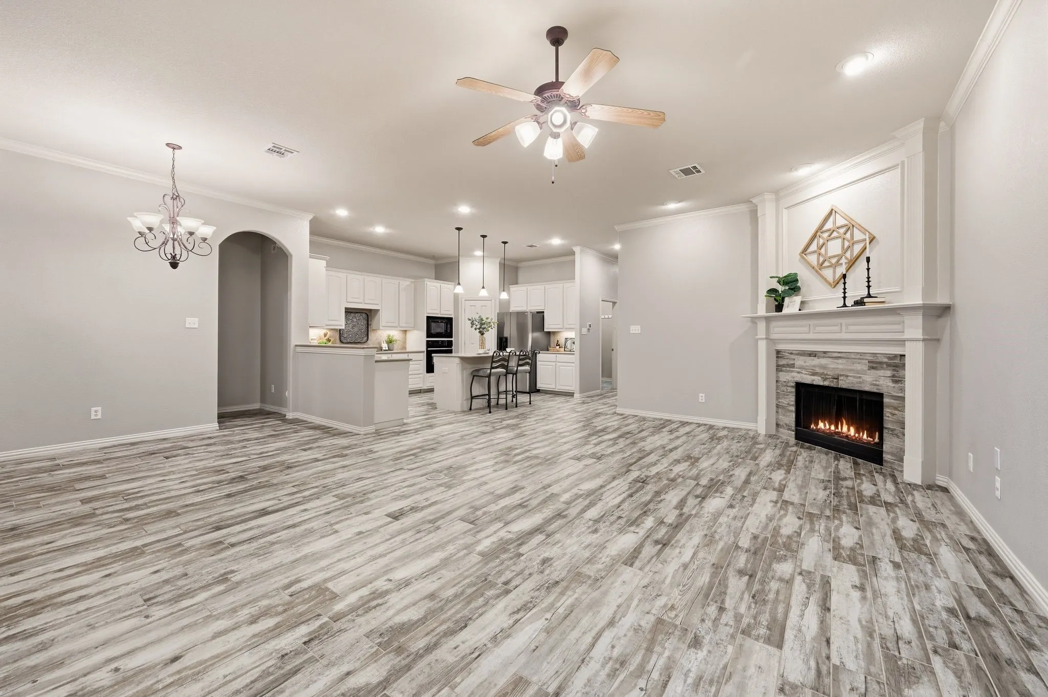 Wood-finish flooring throughout, featuring a fireplace with stone surround and mantle, crown molding, a ceiling fan, and recessed lighting