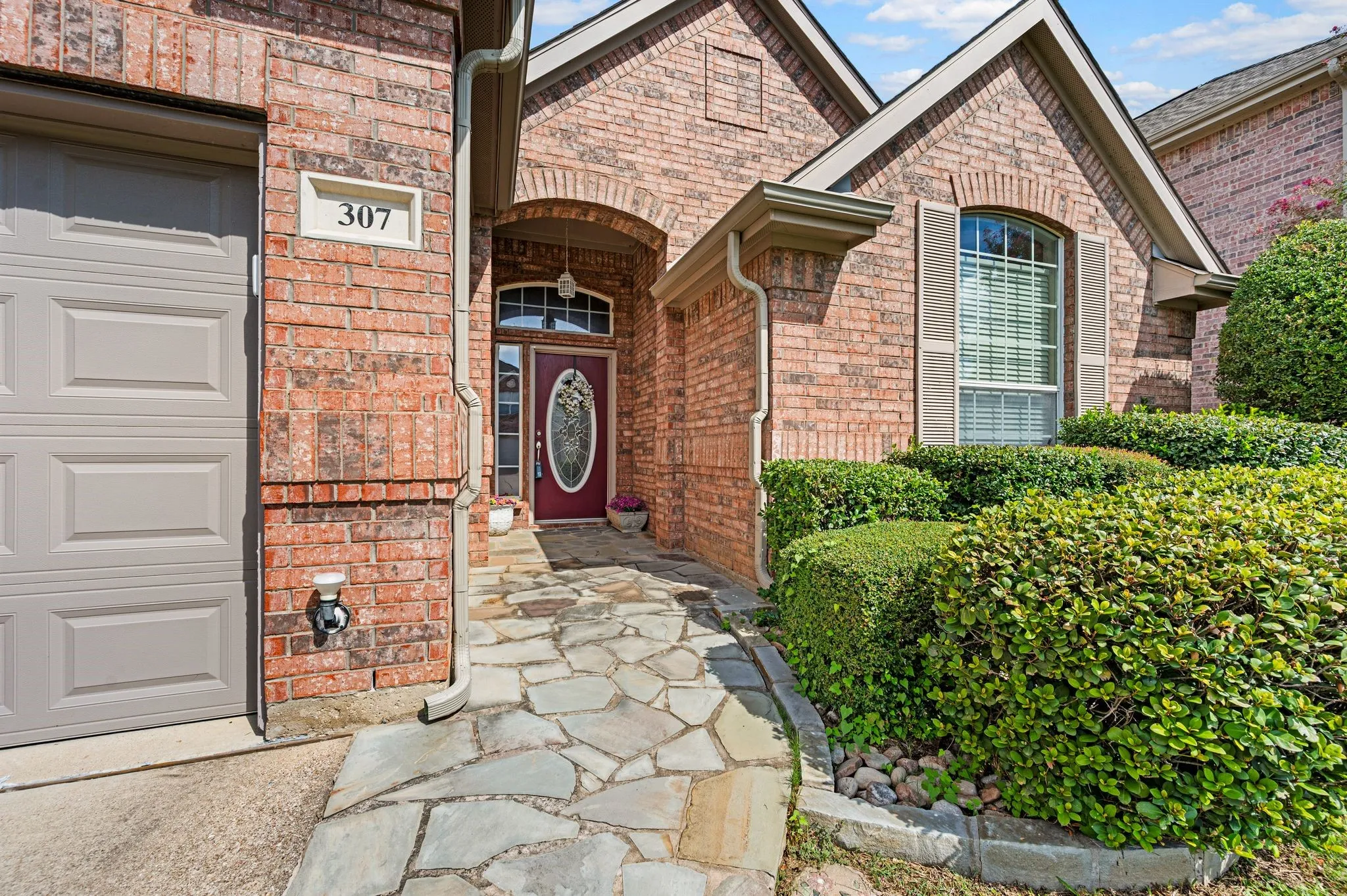 Brick exterior with a stone-finish walkway, arched entry, decorative front door, and garage access