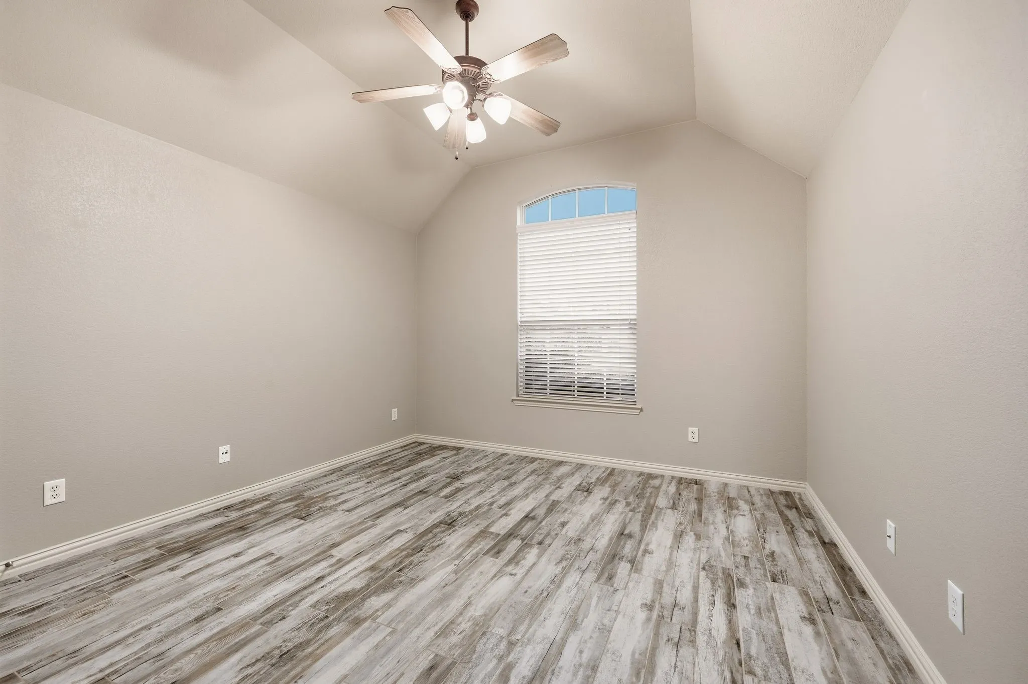 Vaulted ceiling with an attached ceiling fan, wood-finish flooring, and an arched window