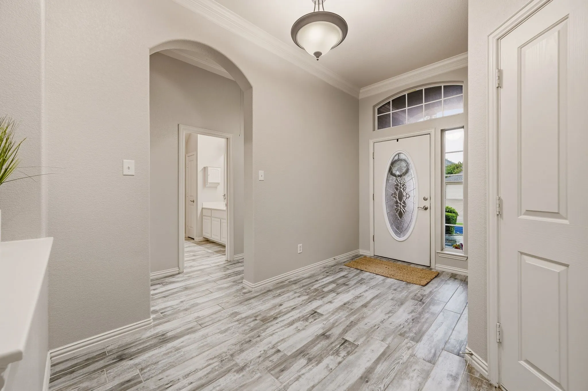 Welcoming entryway showcasing wood-finish plank flooring, arched architectural details, and abundant natural light from transom-topped entry door