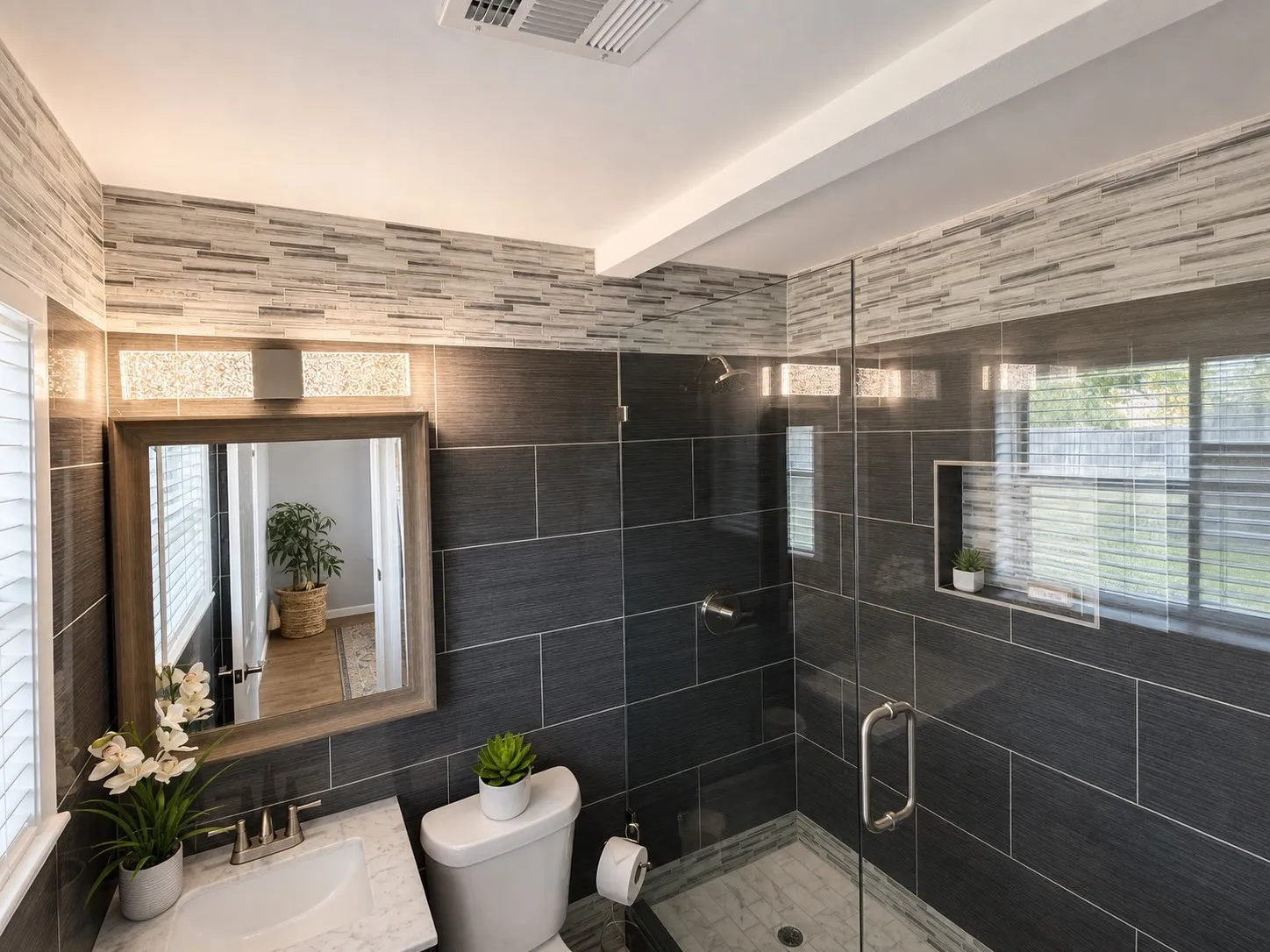 Bathroom featuring a glass-enclosed shower, dark tile shower surround, built-in shower niche, and a vanity with a rectangular sink and framed mirror
