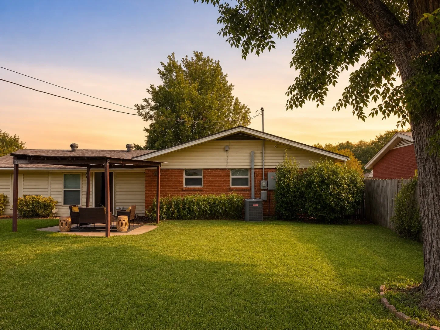 Expansive backyard featuring a manicured lawn, brick and siding exterior, a covered patio, and mature trees