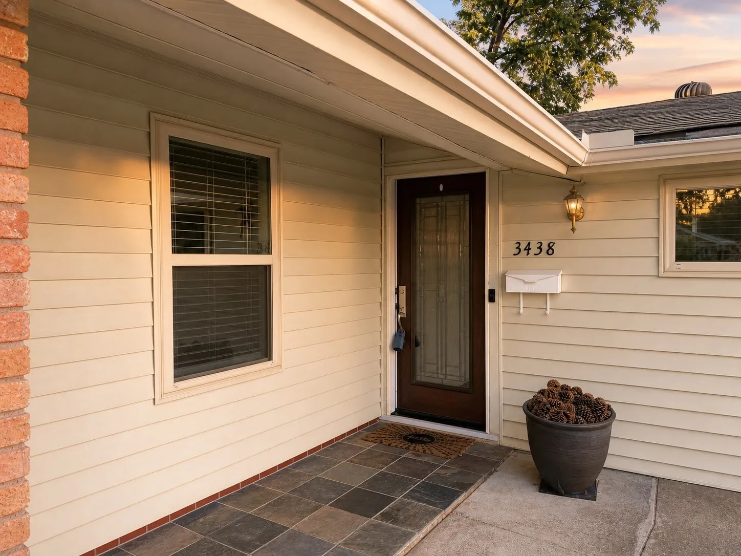 Entryway featuring a dark wood-finish door with decorative glass, cream-colored siding, and a brick accent wall