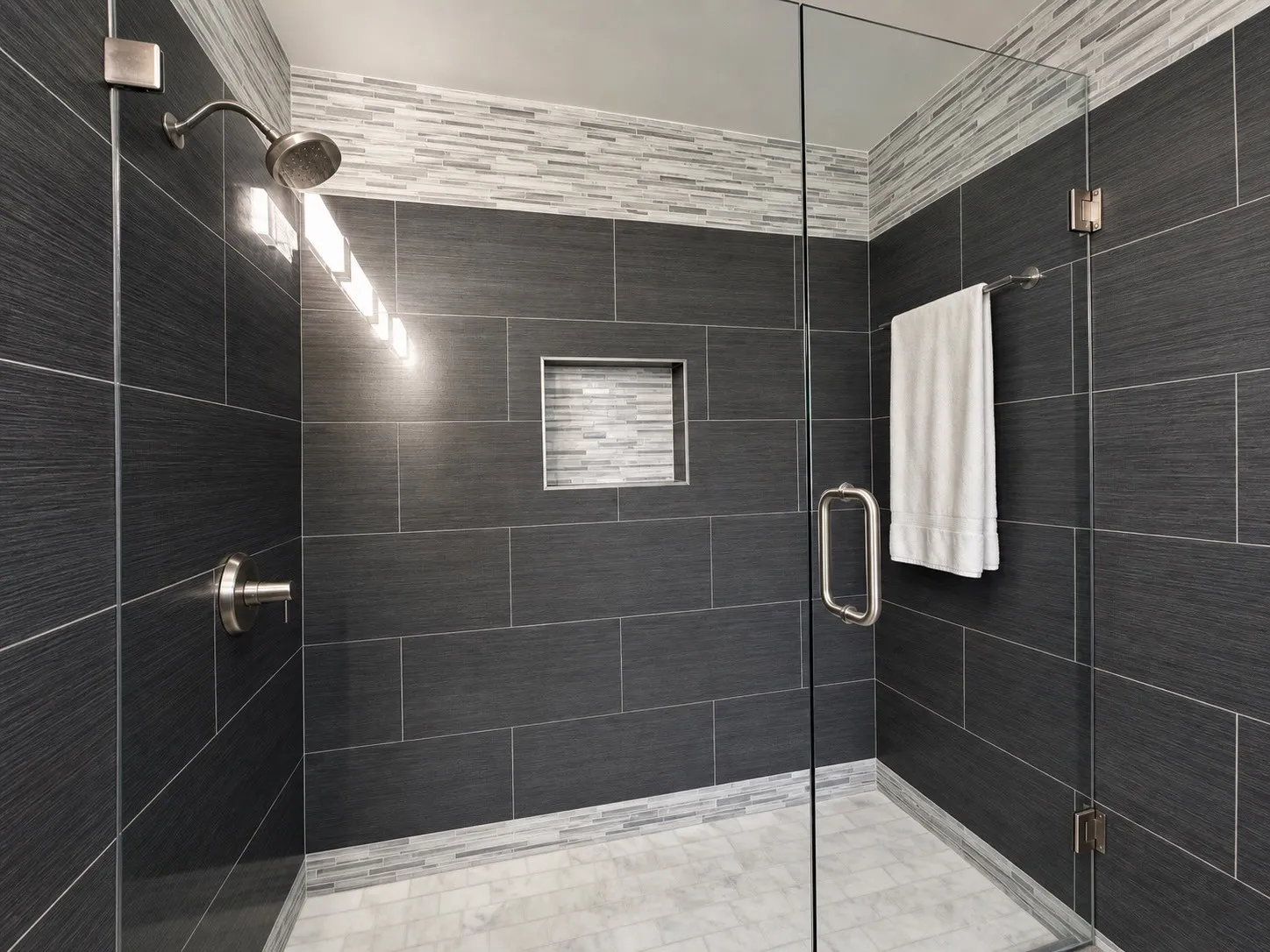 Glass-enclosed shower featuring dark textured tile walls, a mosaic tile accent band, a recessed niche, and a tiled floor