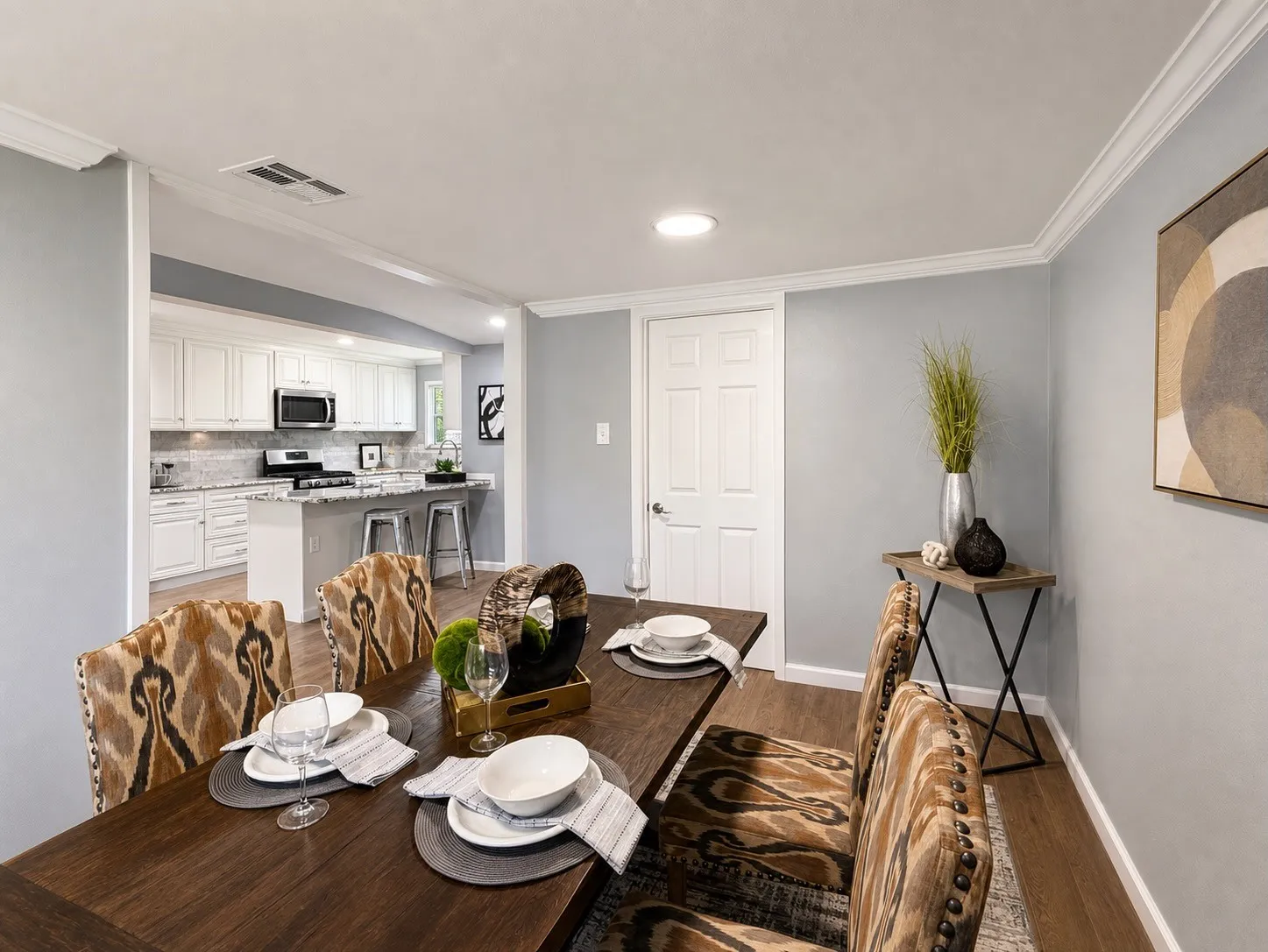 Wood-finish flooring, crown molding, recessed lighting, white panel door, and a kitchen featuring white cabinetry, light countertops, and stainless steel appliances