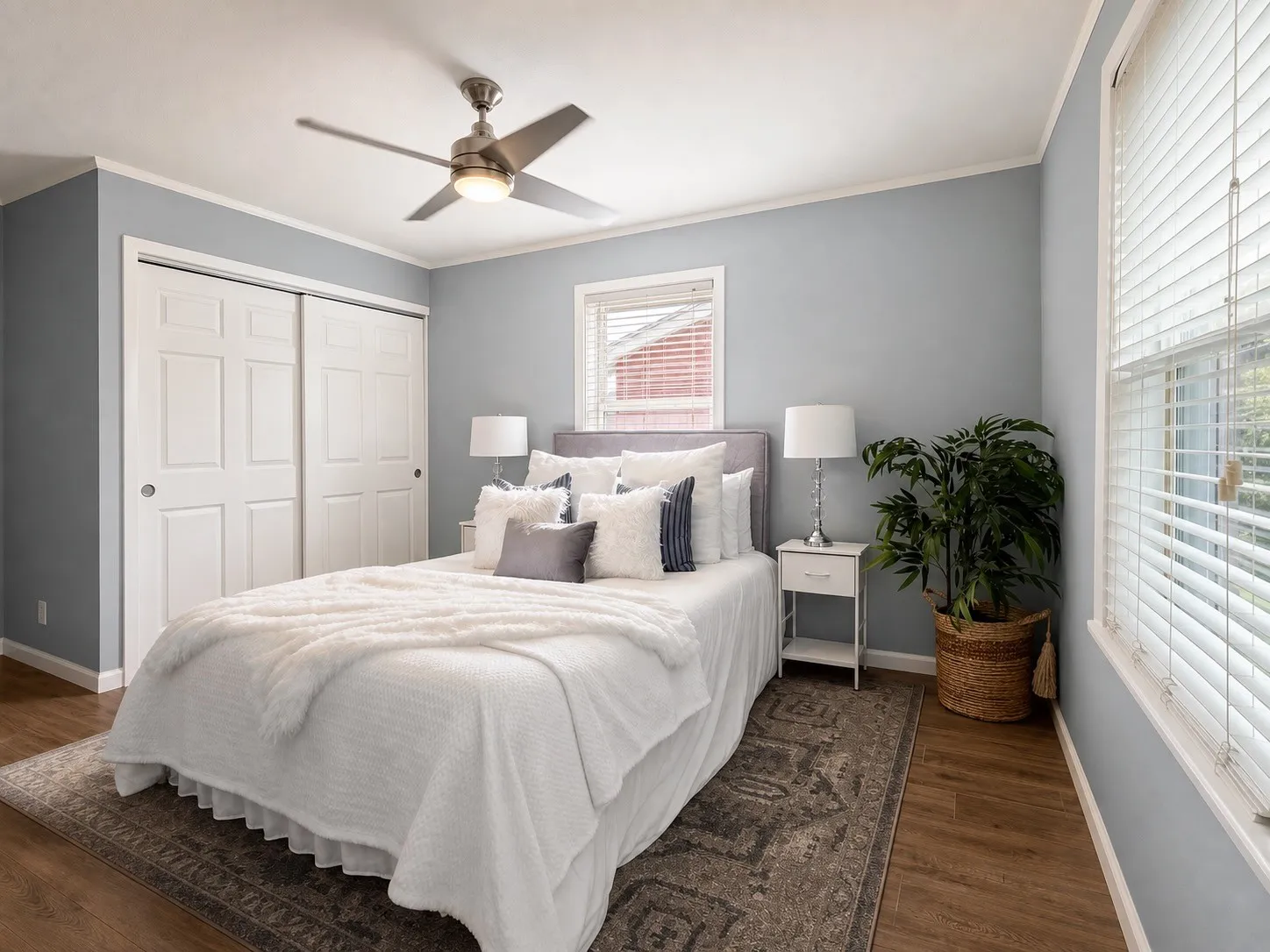 Wood-finish flooring, light blue wall paint, white trim, sliding closet doors, and a ceiling fan