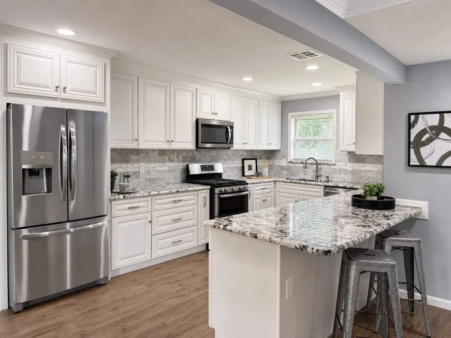 Well-appointed kitchen featuring white cabinetry, stainless steel appliances, speckled stone countertops, a tiled backsplash, and wood-finish flooring