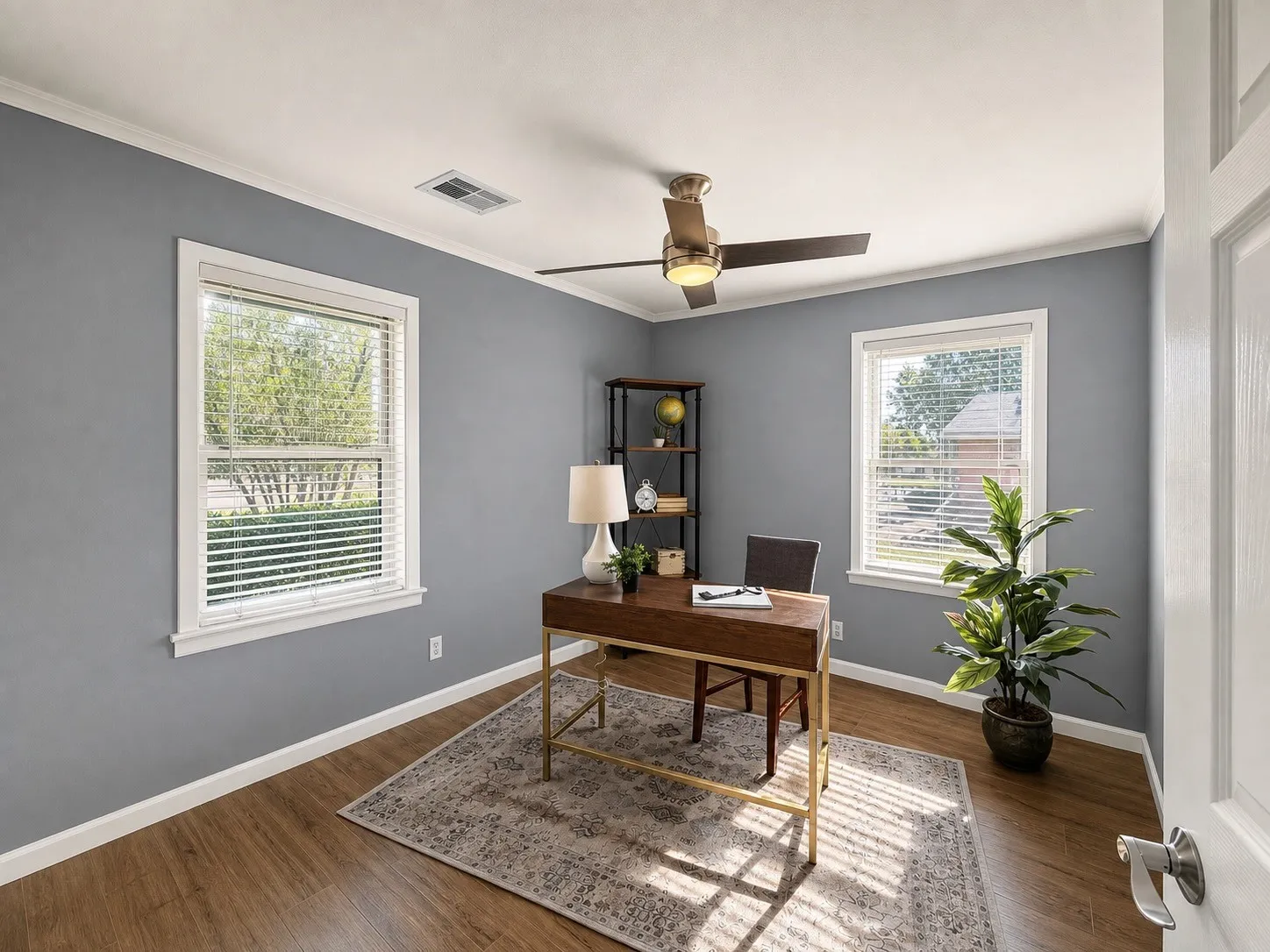 Wood-finish flooring, crown molding, two windows with blinds, and a ceiling fan with integrated lighting