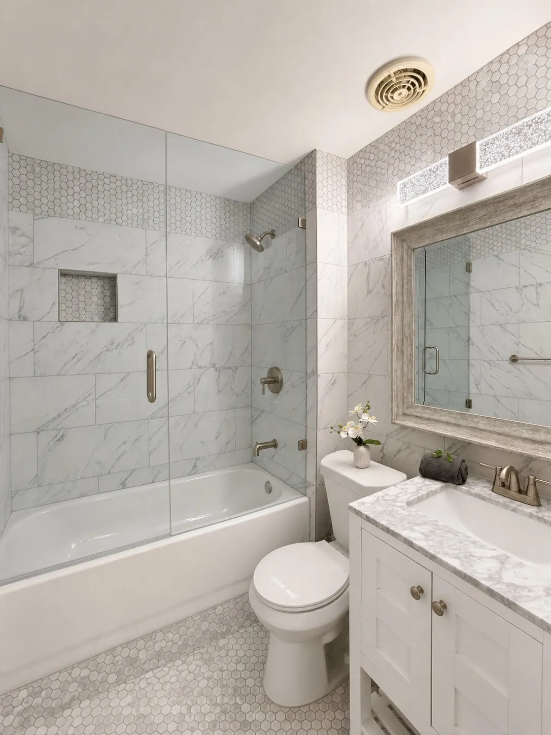 Bathroom featuring a white vanity with a marble-finish countertop, a tub with a glass enclosure, and honeycomb tile flooring