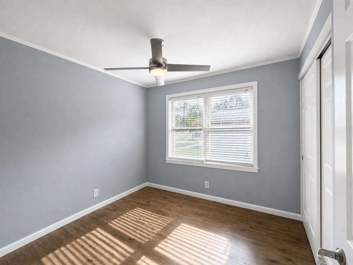 Wood-finish flooring, white trim, a modern ceiling fan, and a window with blinds