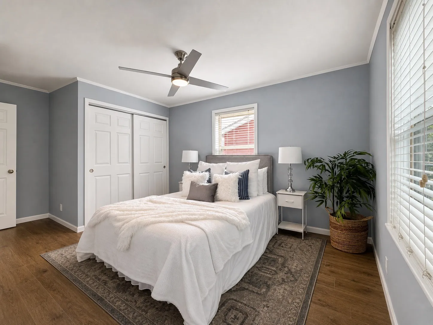 Wood-finish flooring, two large paneled closet doors, ceiling fan with integrated lighting, and multiple windows with blinds