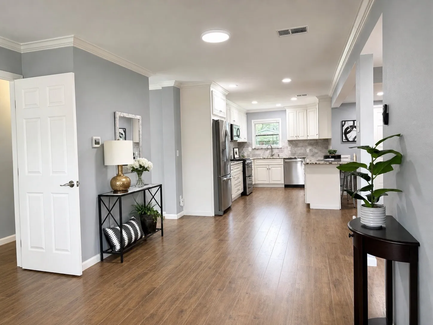 Wood-finish flooring, crown molding, a kitchen with white cabinetry, stainless steel appliances, and a kitchen island with seating