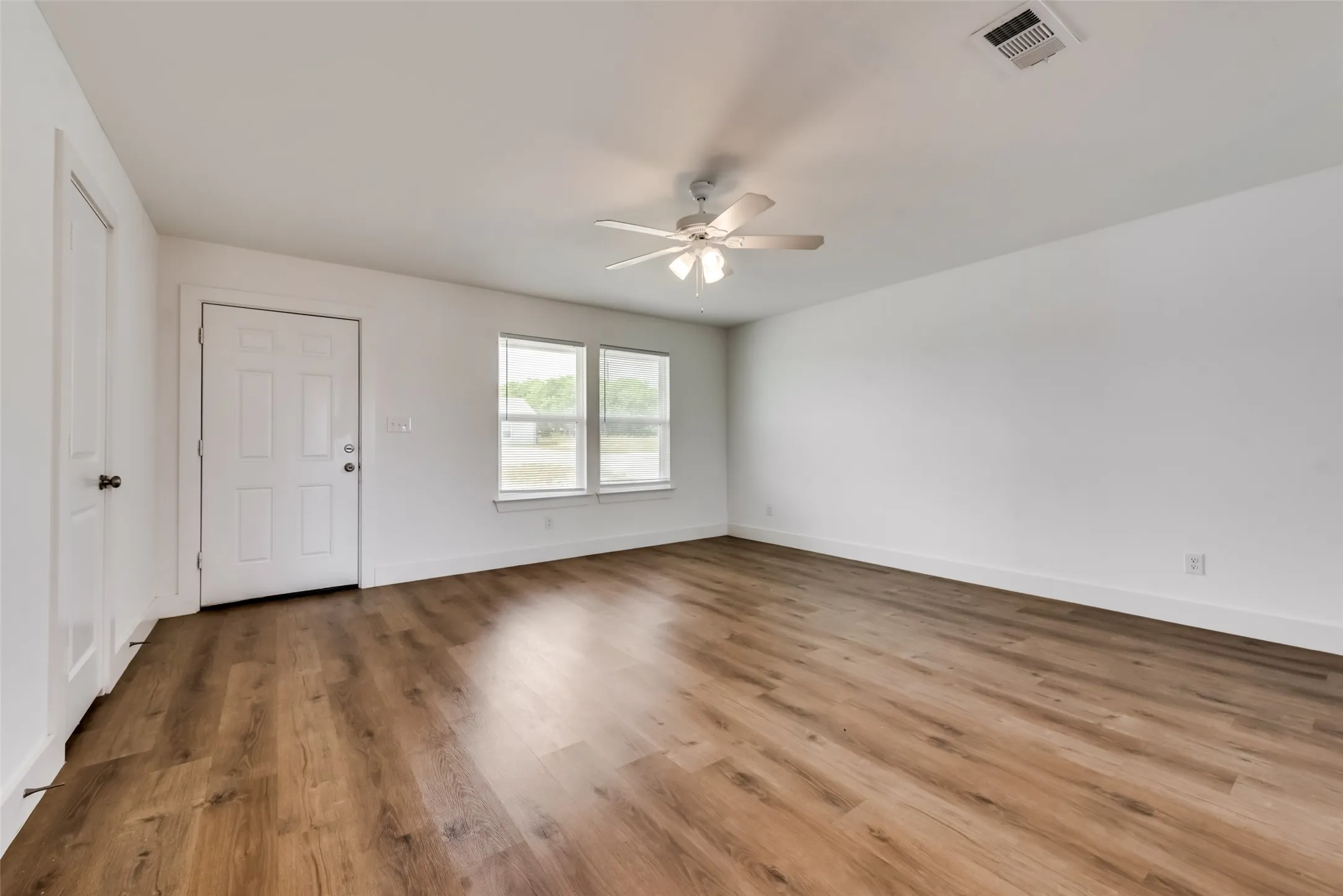 Spacious room with wood-finish flooring, white walls, and a ceiling fan