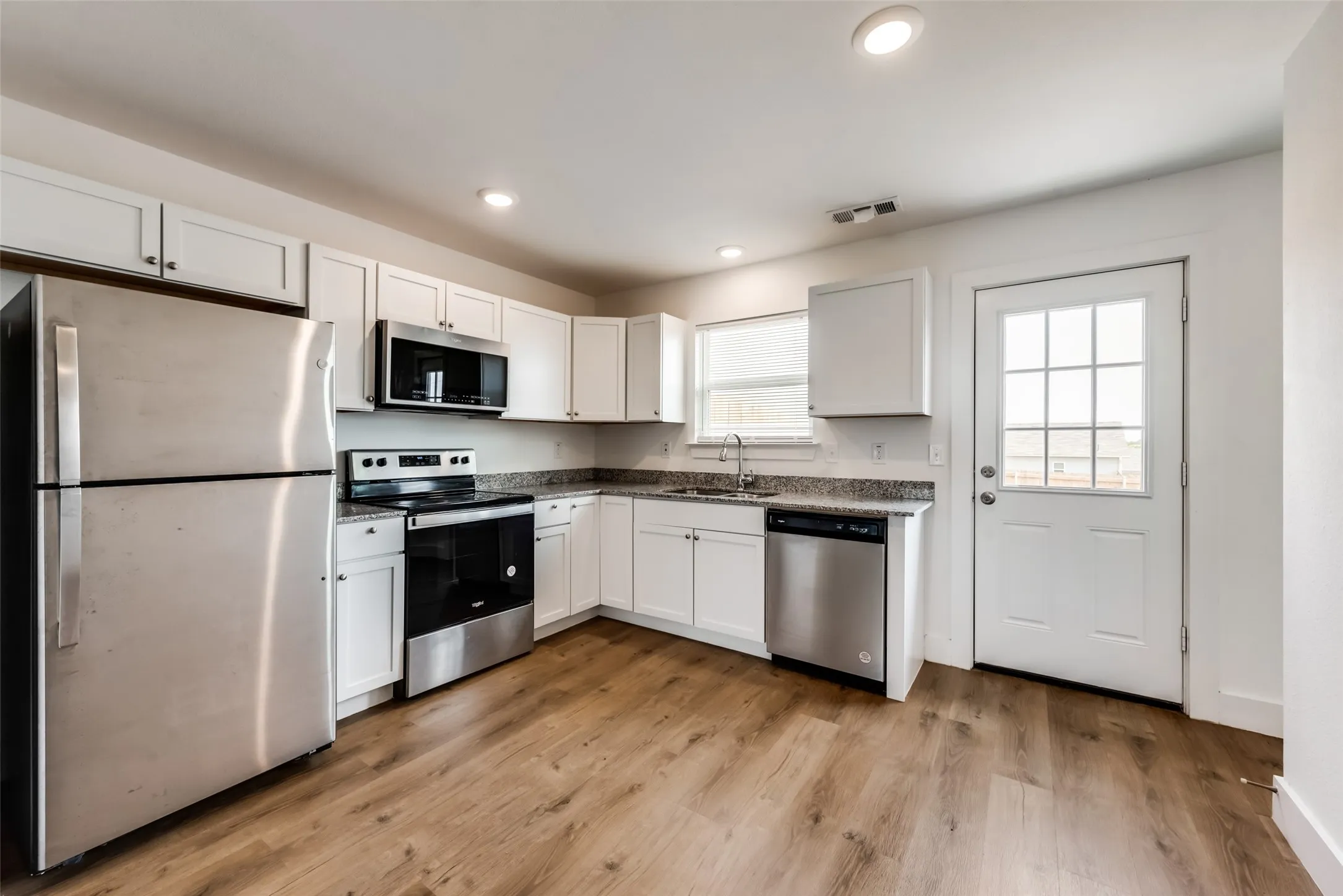 Kitchen featuring white cabinetry, wood-finish flooring, stainless steel appliances, recessed lighting, and a glass-paned door