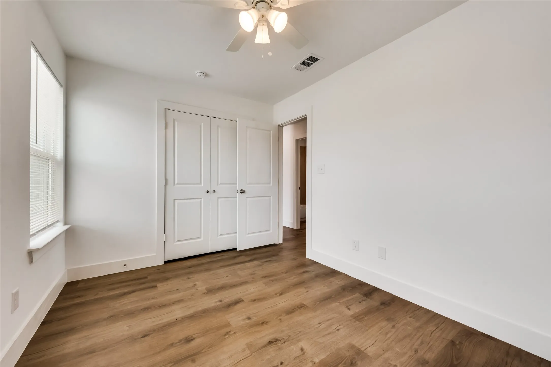 Wood-finish flooring throughout, white interior walls, and a ceiling fan with light fixture