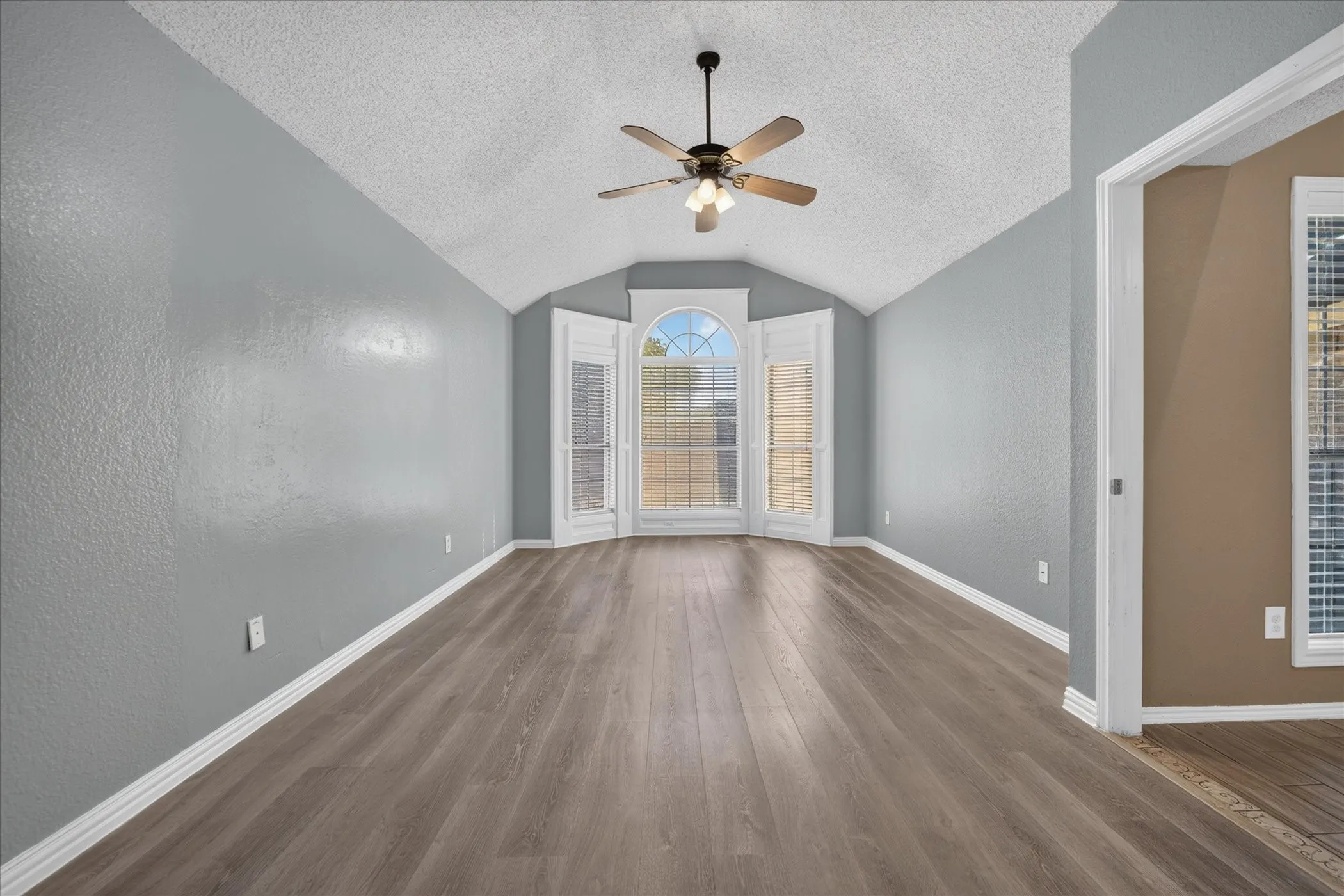 Vaulted ceiling with a ceiling fan, wood-finish flooring, and bay window with arched transom