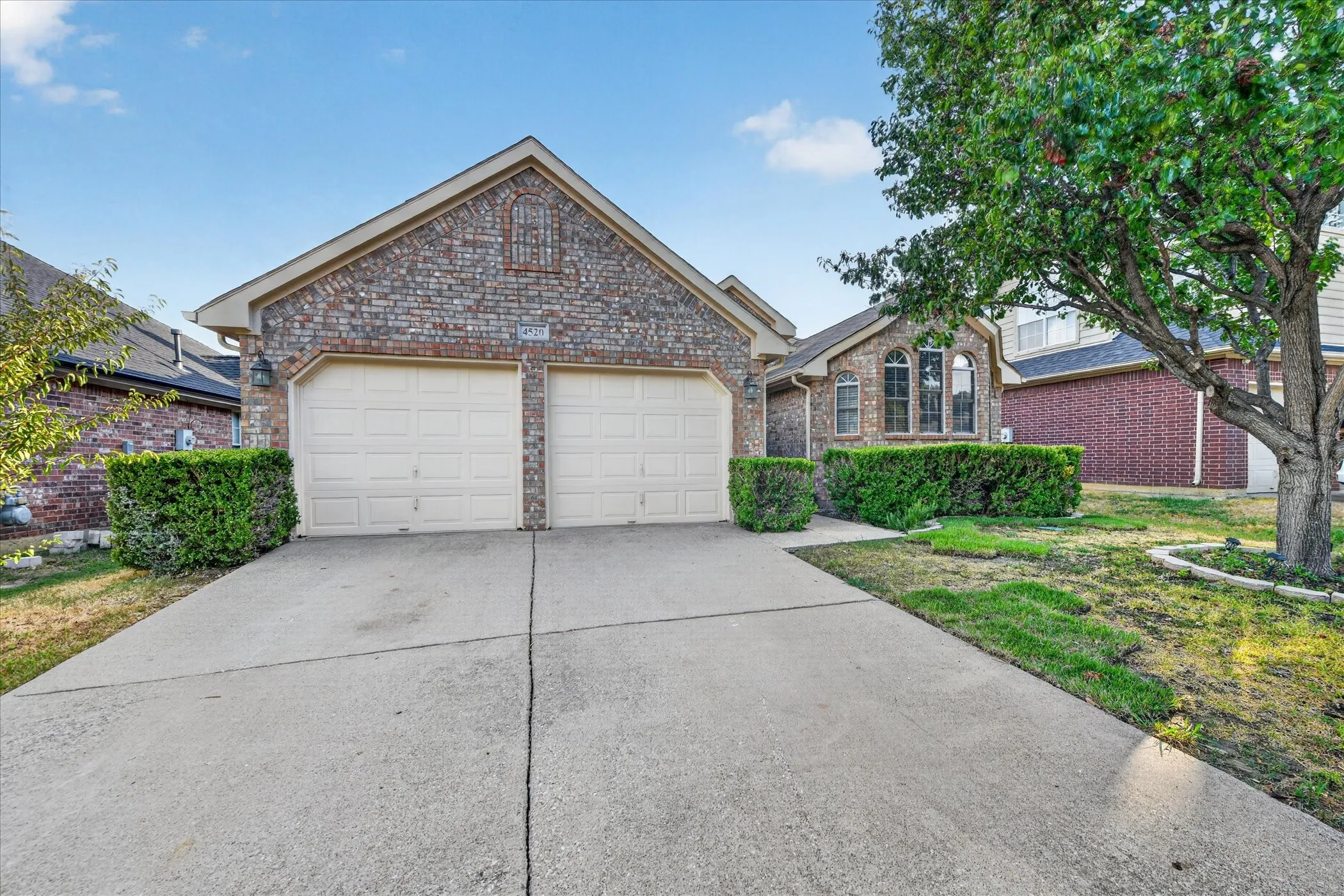 Brick exterior with a gabled roofline, two-car garage, concrete driveway, and mature landscaping