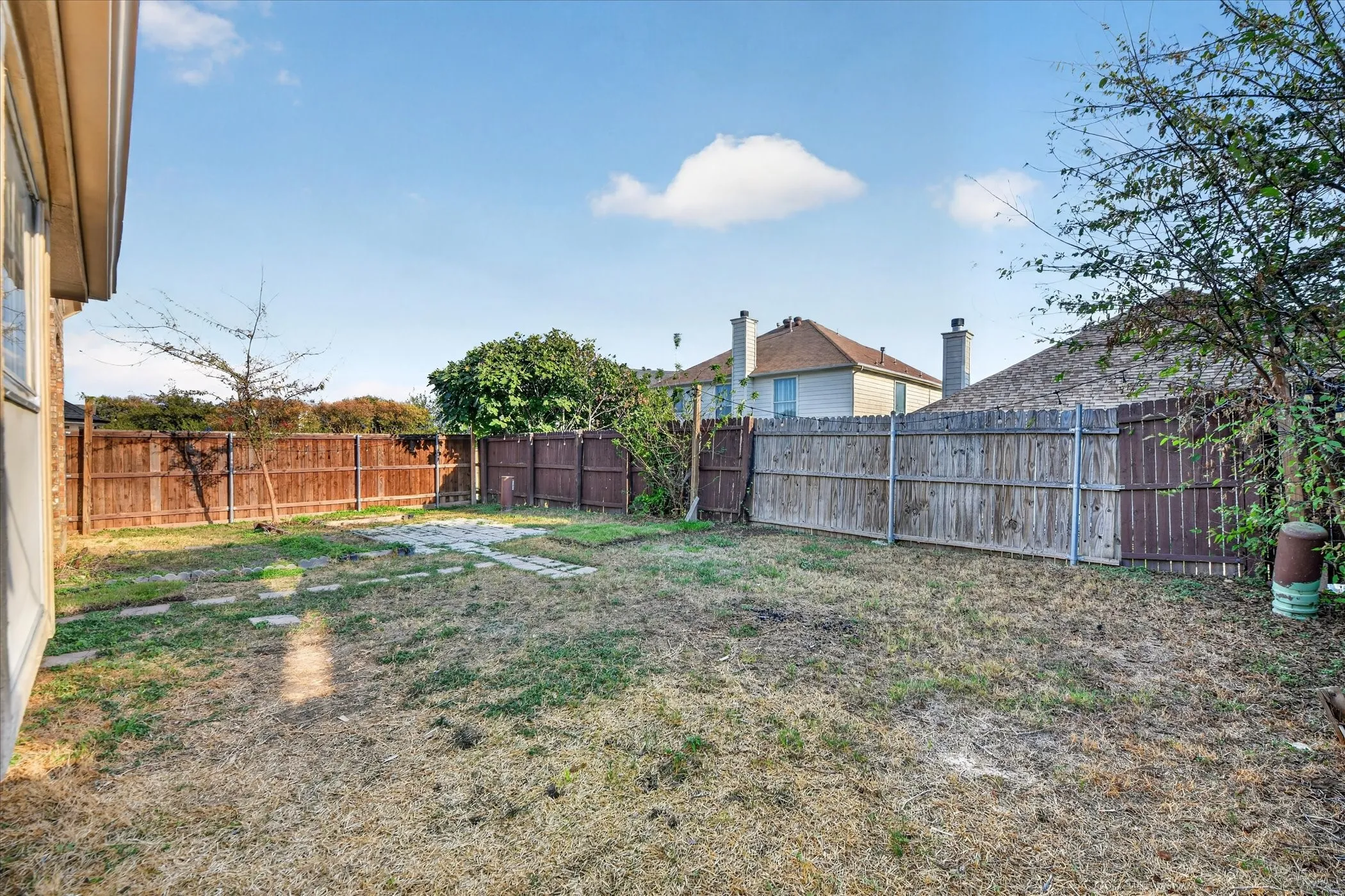 Fenced backyard with a stone pathway and mature trees