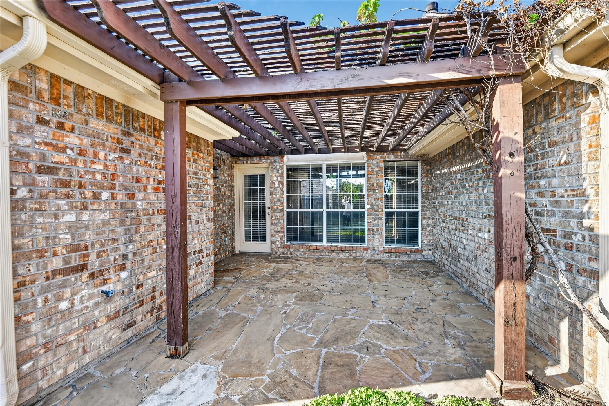Expansive brick patio featuring a wood pergola, irregular flagstone paving, and grid-pattern windows