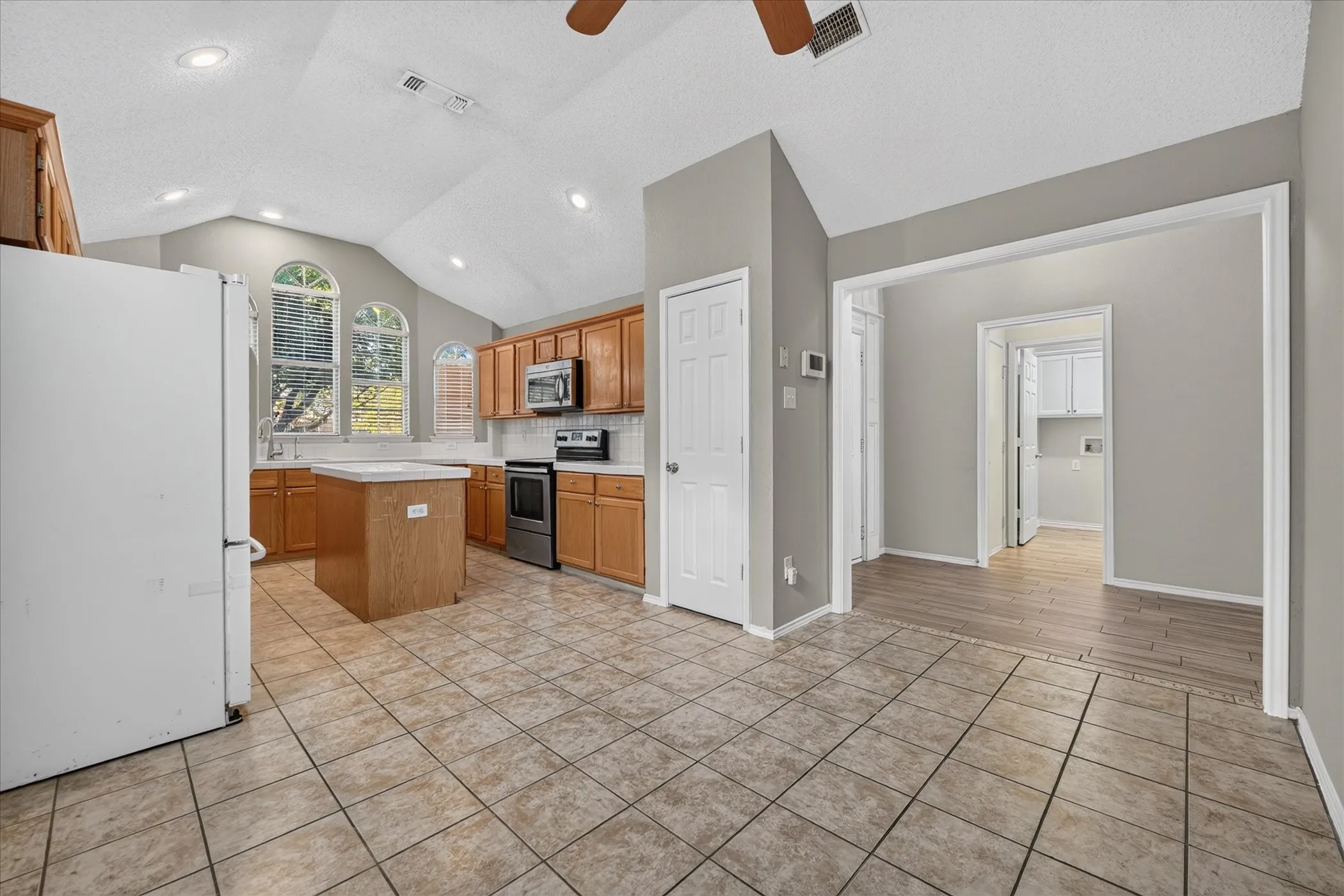 Kitchen featuring a vaulted ceiling, recessed lighting, wood-finish cabinetry, a central island, and arched windows