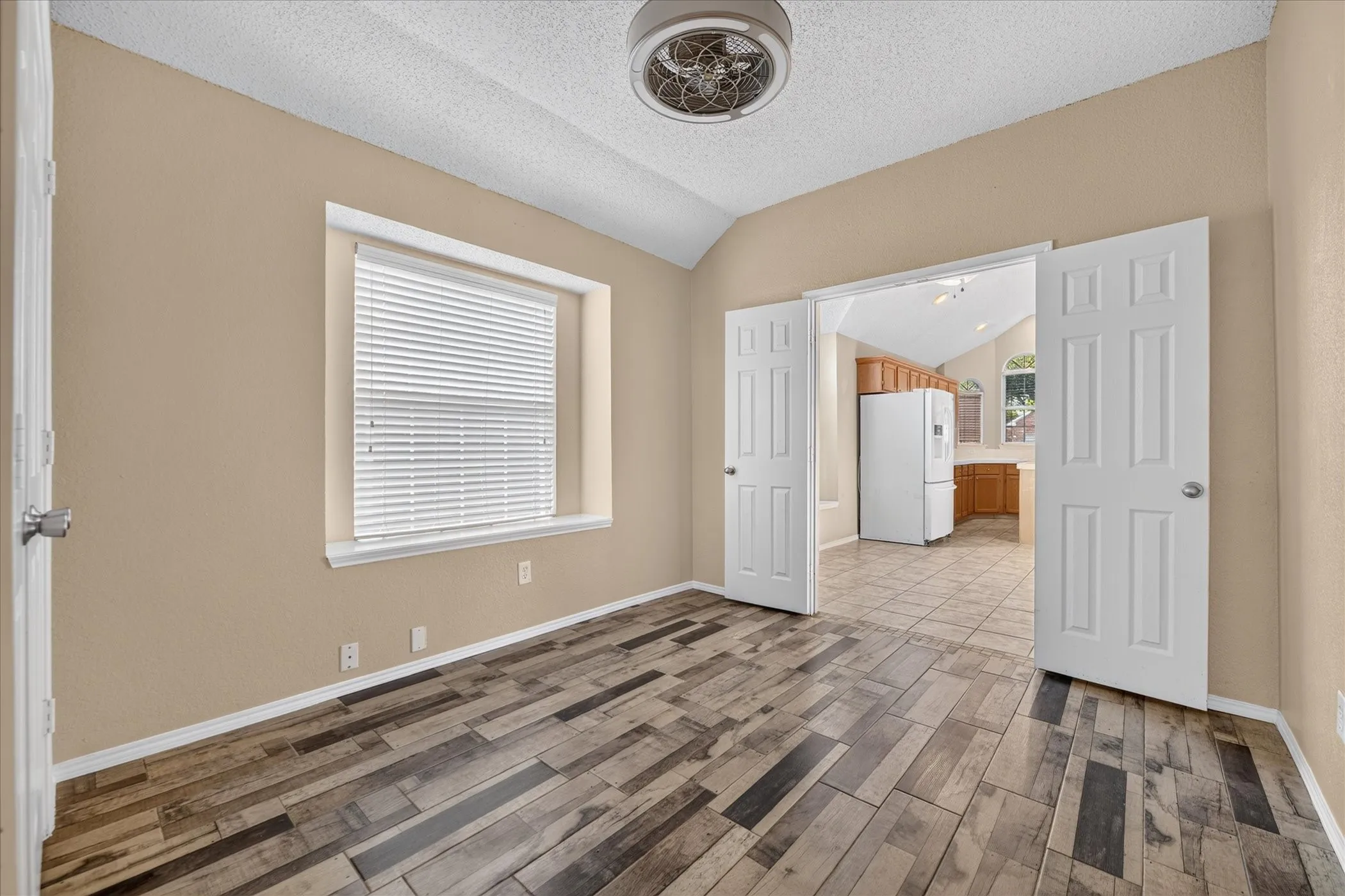 Vaulted ceiling with a flush-mount light fixture, wood-finish flooring, and white trim