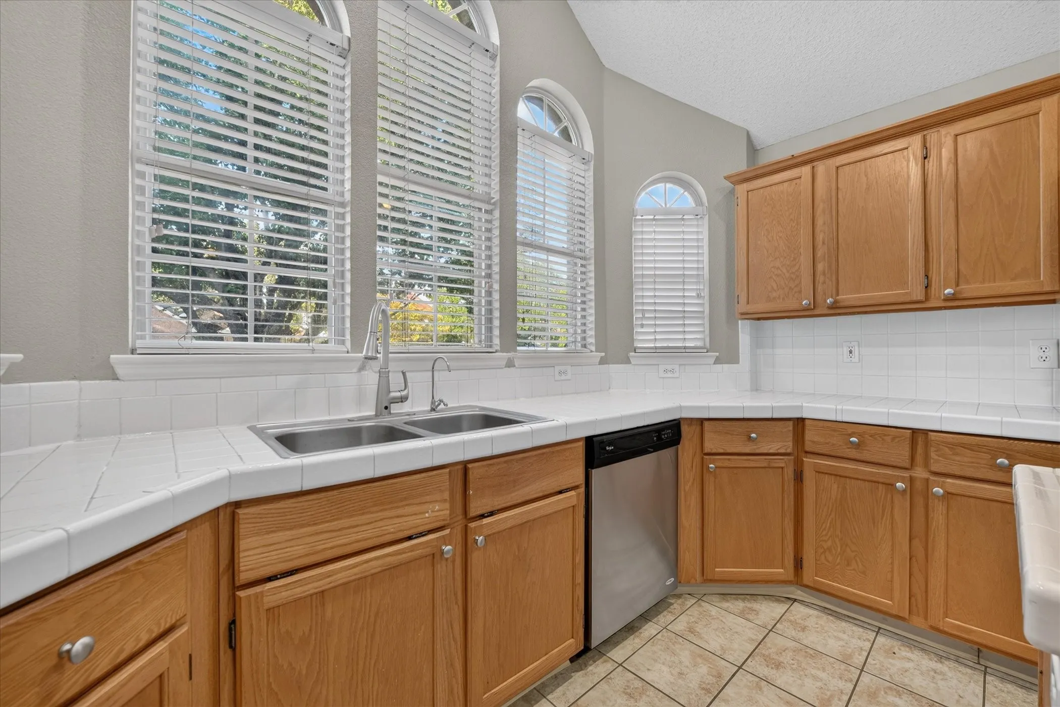 Kitchen featuring wood cabinetry, white tile countertops, stainless steel sink, stainless steel dishwasher, and tiled flooring