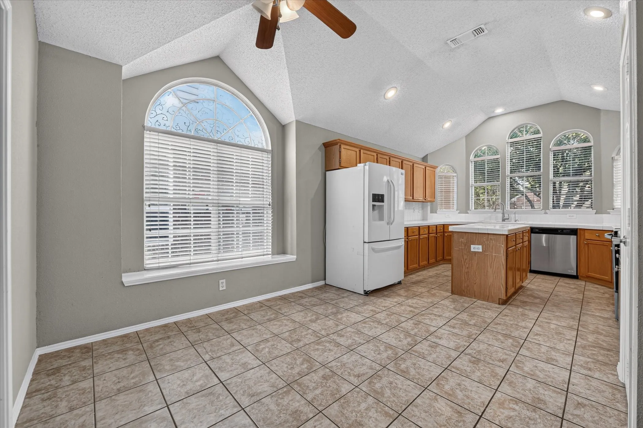 Vaulted ceilings, recessed lighting, arched windows, tile flooring, and wood-finish cabinetry
