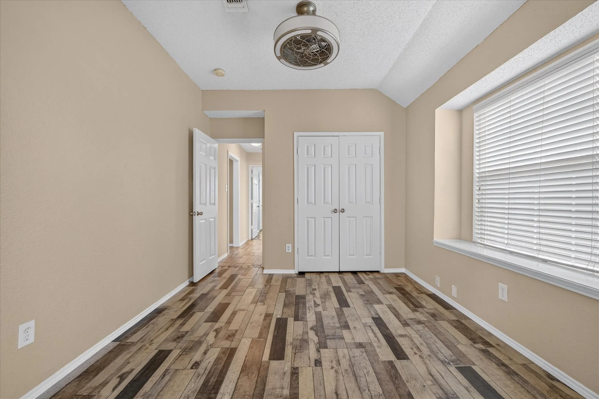 Vaulted ceiling, wood-finish plank flooring, large window with blinds, recessed window ledge, and bi-fold closet doors