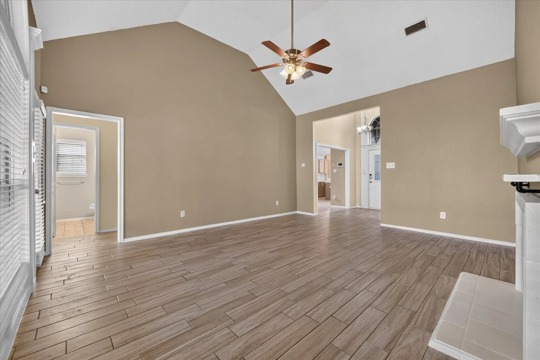Vaulted ceiling with a ceiling fan, wood-finish flooring, white fireplace mantel, and neutral wall paint