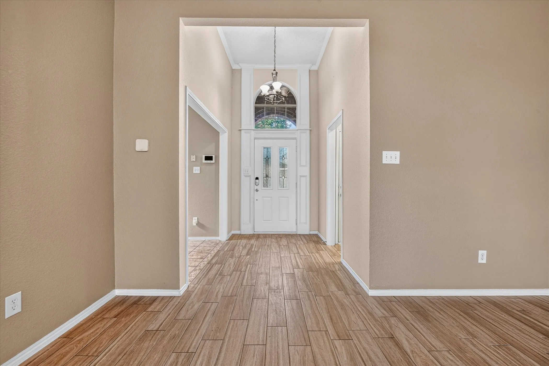 Bright hallway featuring wood-finish flooring, white trim and doors, recessed lighting, and a pendant fixture above the entrance
