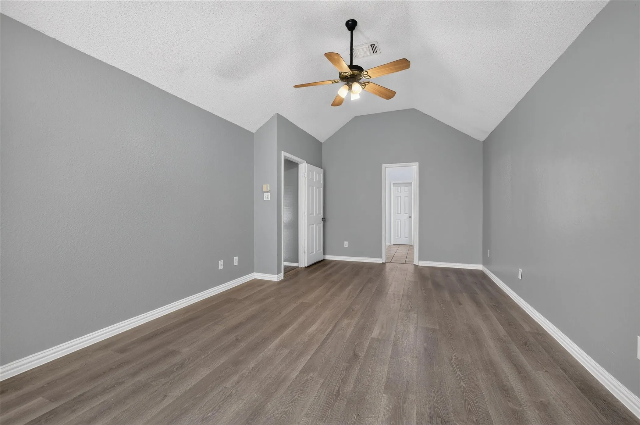 Vaulted ceiling, wood-finish flooring, ceiling fan with integrated lighting, neutral wall tones, white trim