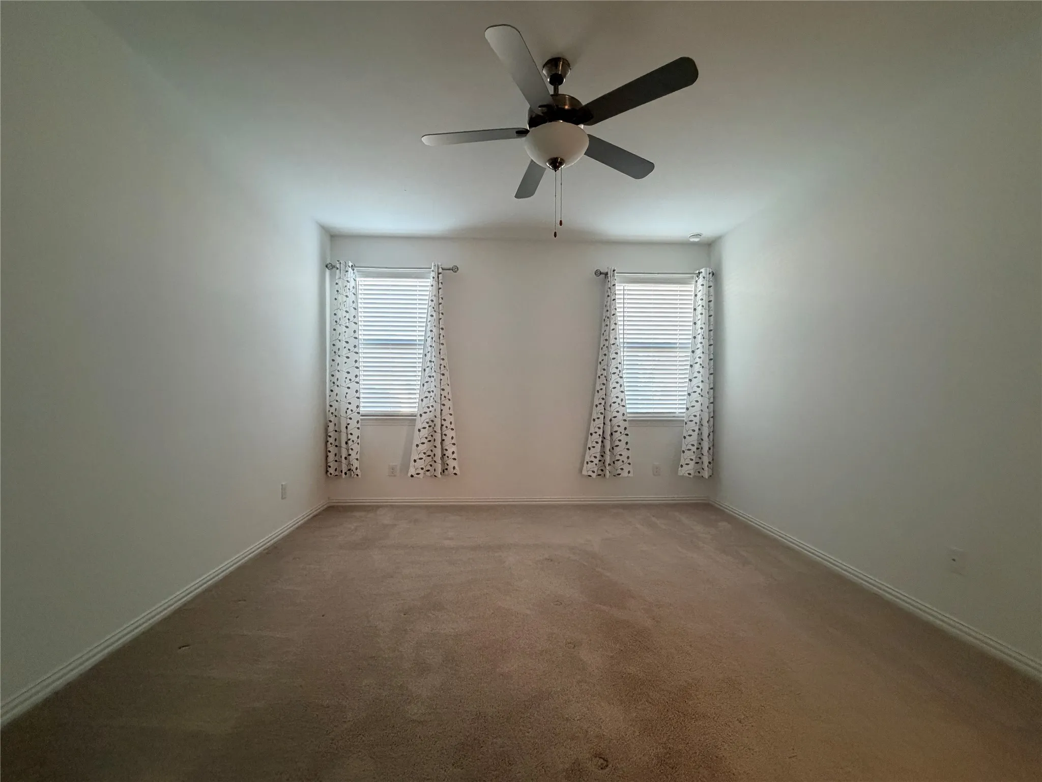 Neutral-toned carpeting, two windows with blinds, and a ceiling fan with integrated lighting