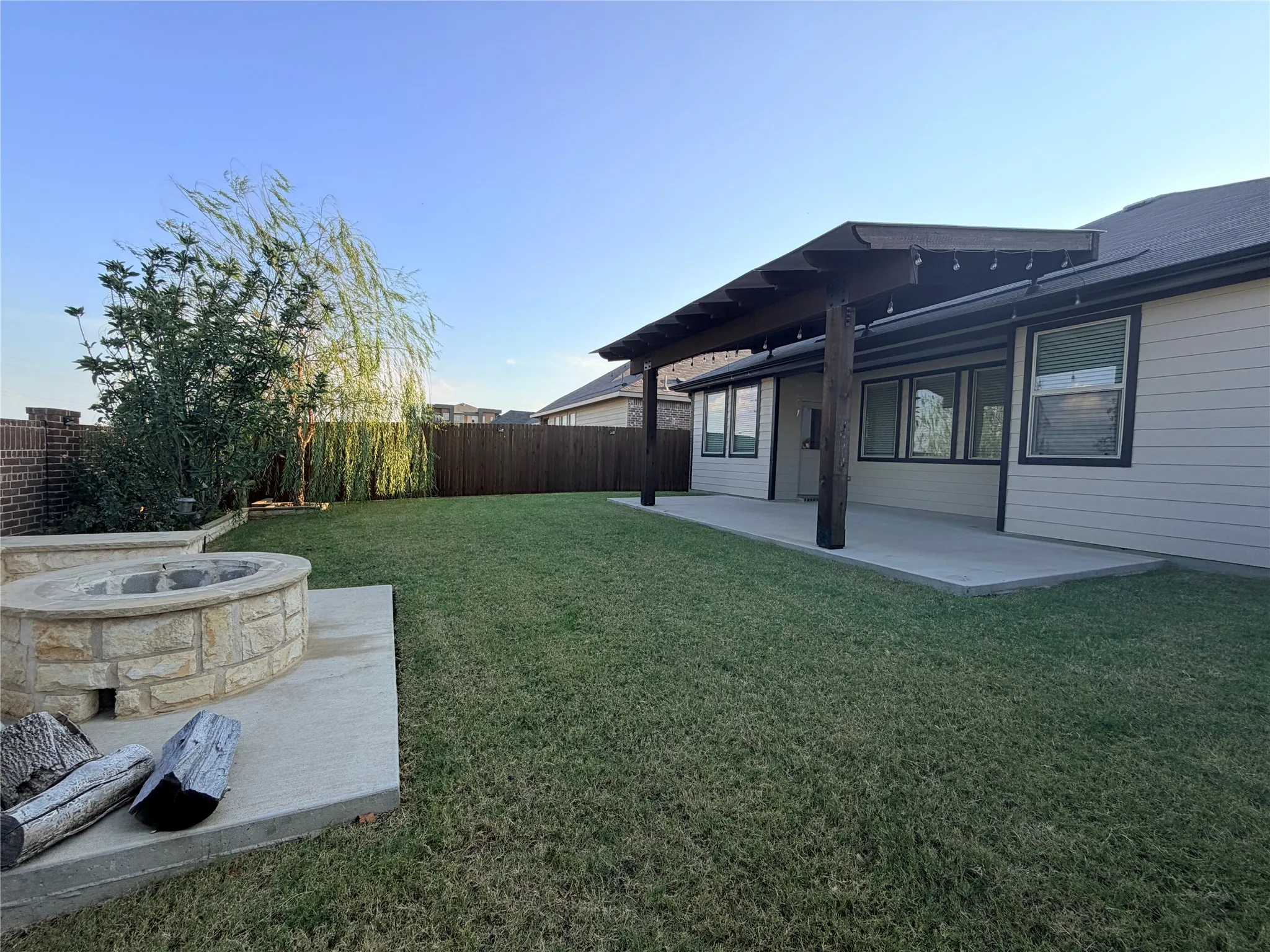 Expansive backyard featuring a stone-clad fire pit, extended concrete patio, and a covered pergola