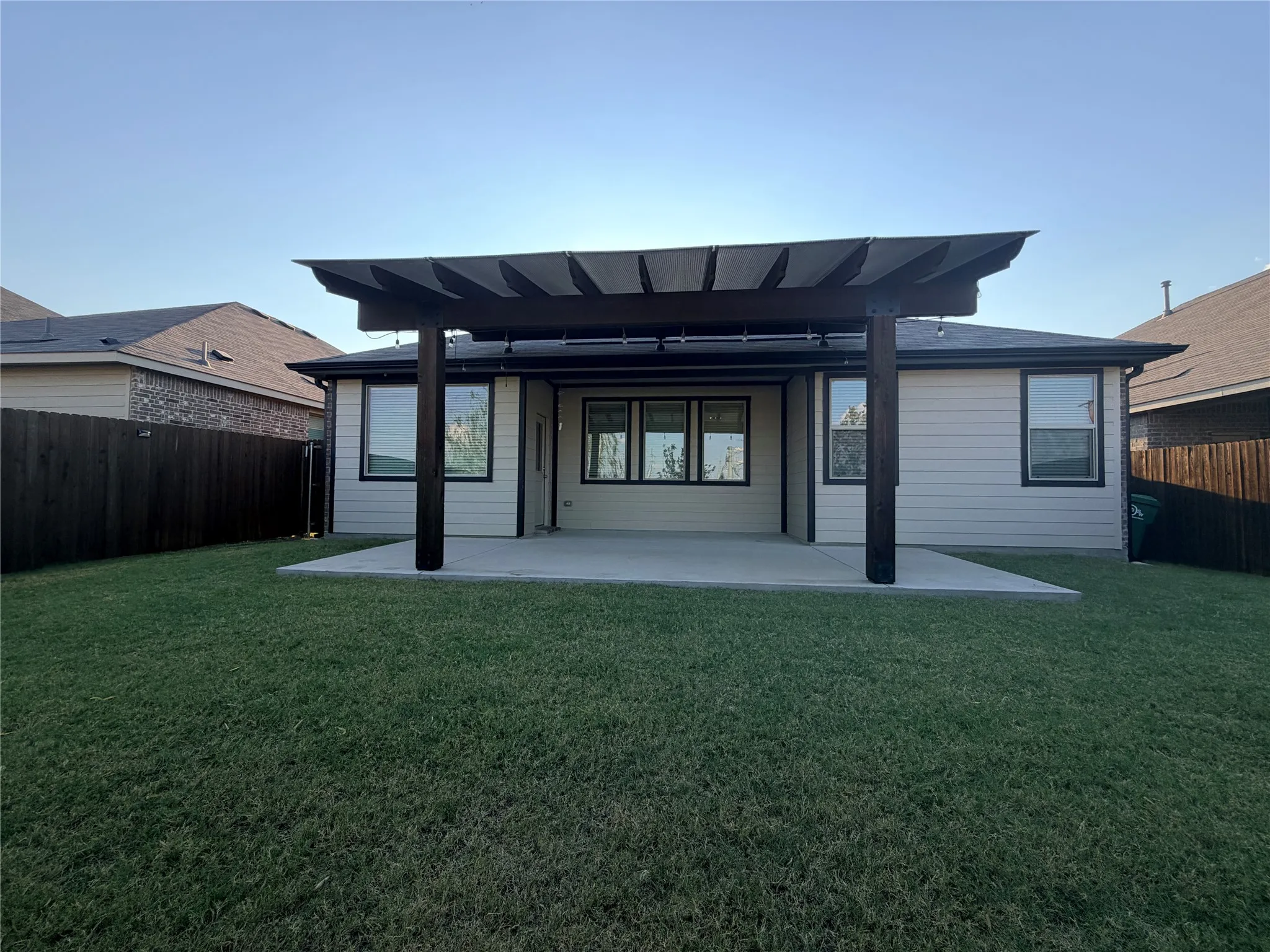 Expansive backyard featuring a concrete patio, a dark wood pergola, and a dark wood privacy fence